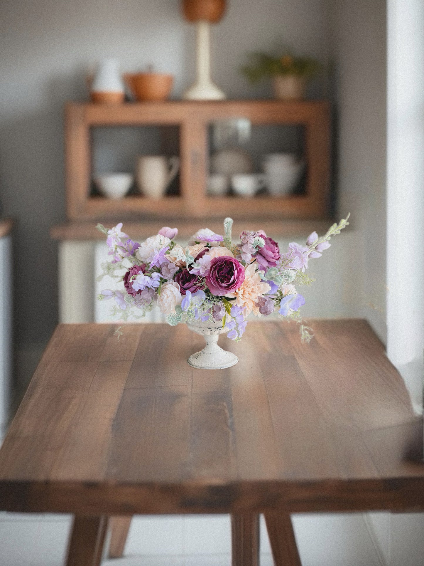 Floral arrangement in a white vase on a wooden table with a blurred background