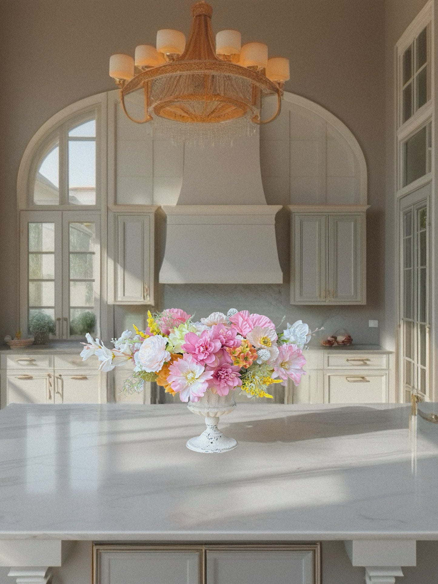 Kitchen with a floral arrangement on a counter, elegant chandelier, and large windows.