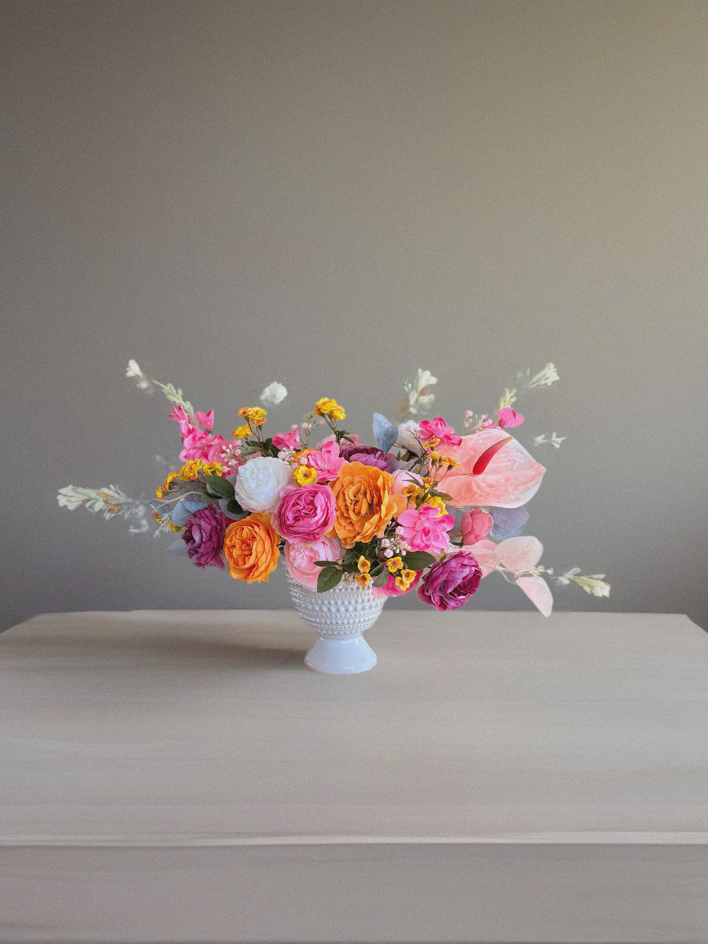 Colorful flower arrangement in a white vase on a gray surface with a neutral background