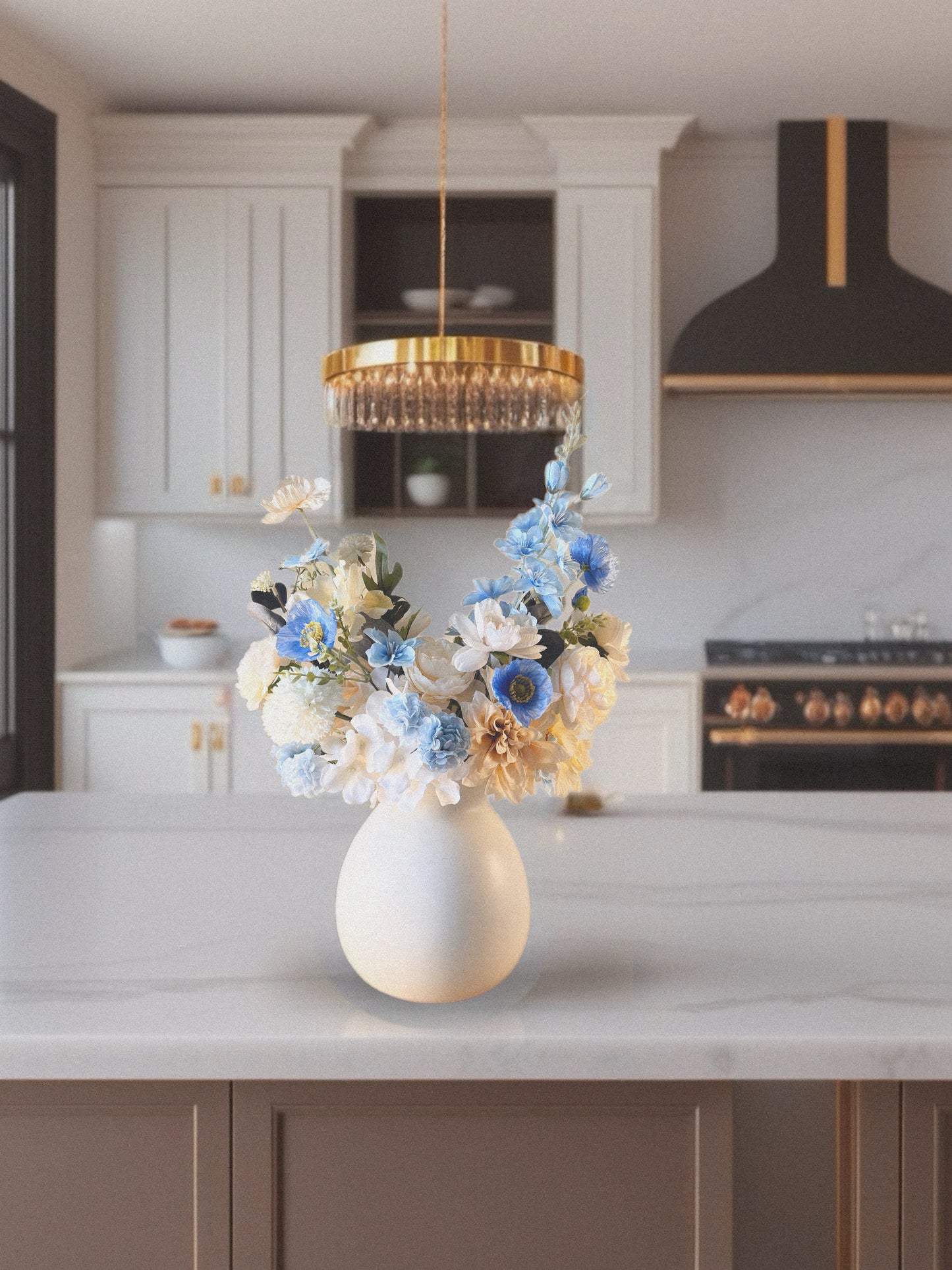 Decorative flowers in a white vase on a kitchen counter with a modern chandelier above.