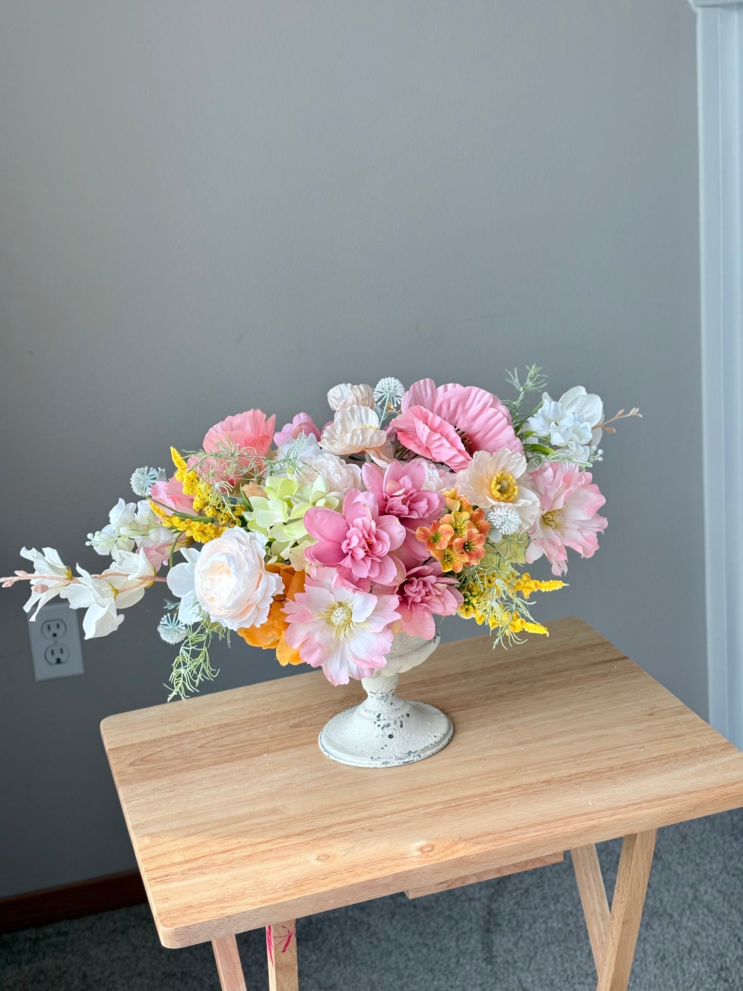 Floral arrangement in a white vase on a wooden table against a gray wall.