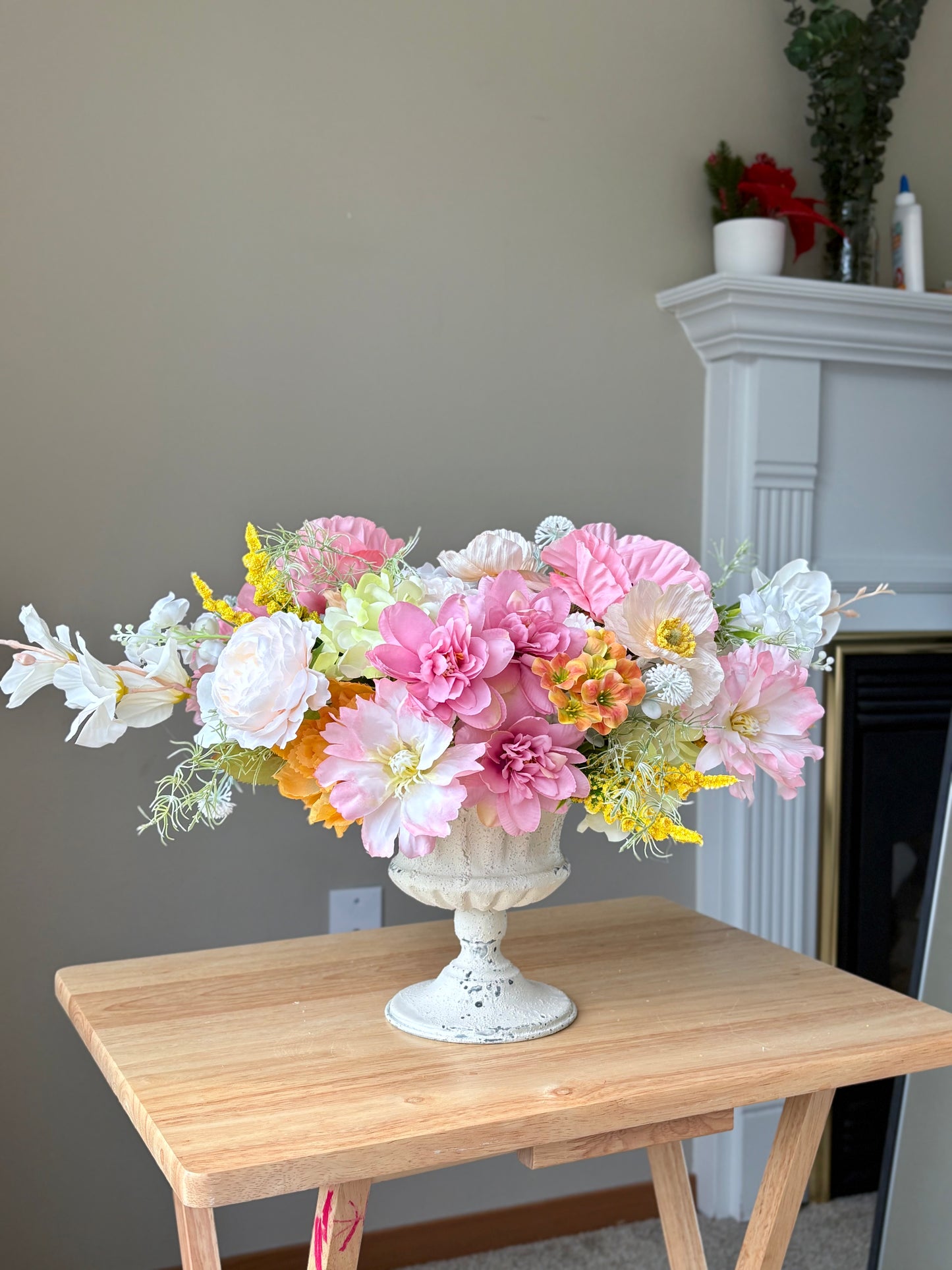 Floral arrangement in a decorative vase on a wooden table with a fireplace in the background.