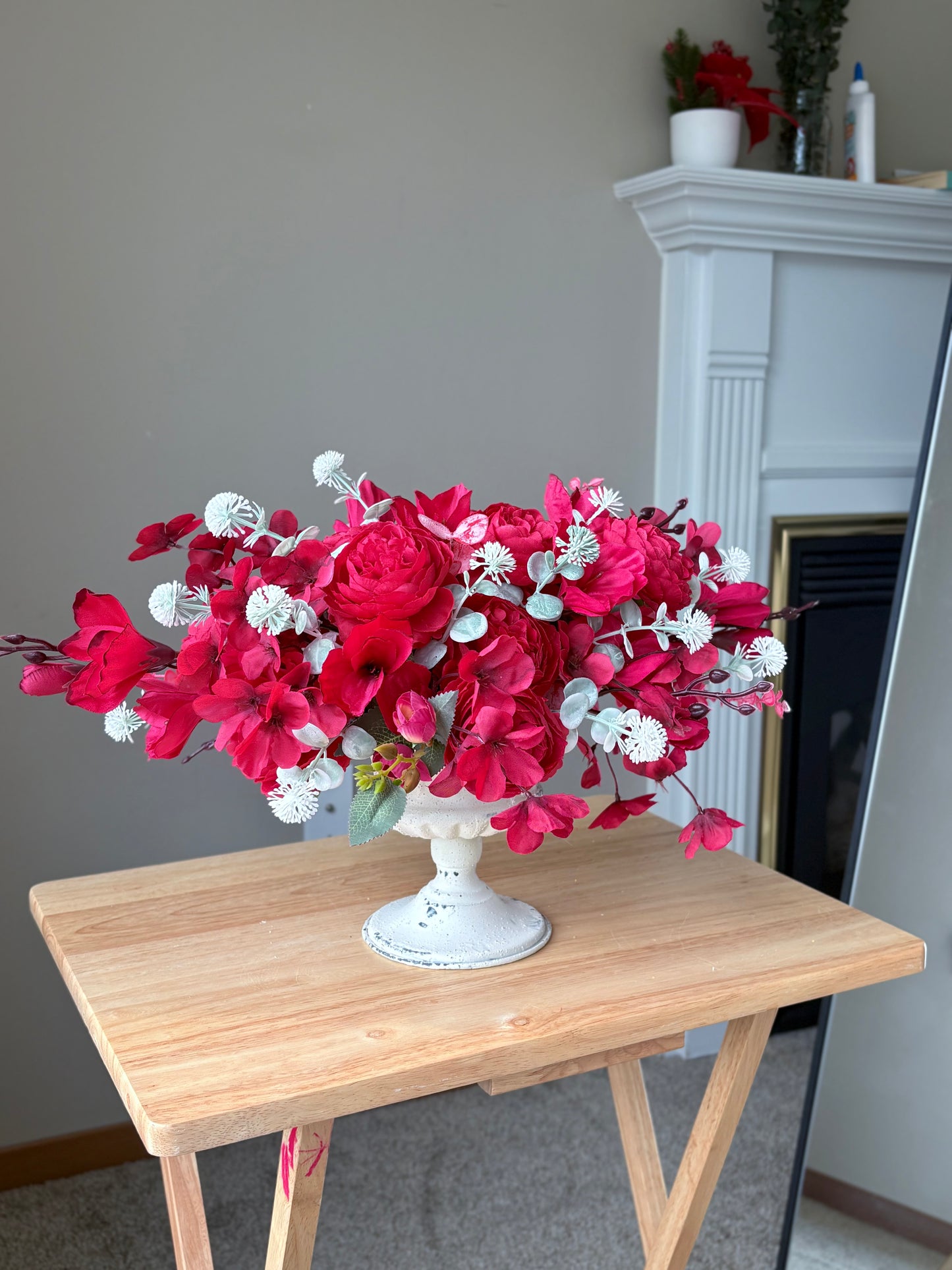Bouquet of red and white flowers in a white vase on a wooden table.