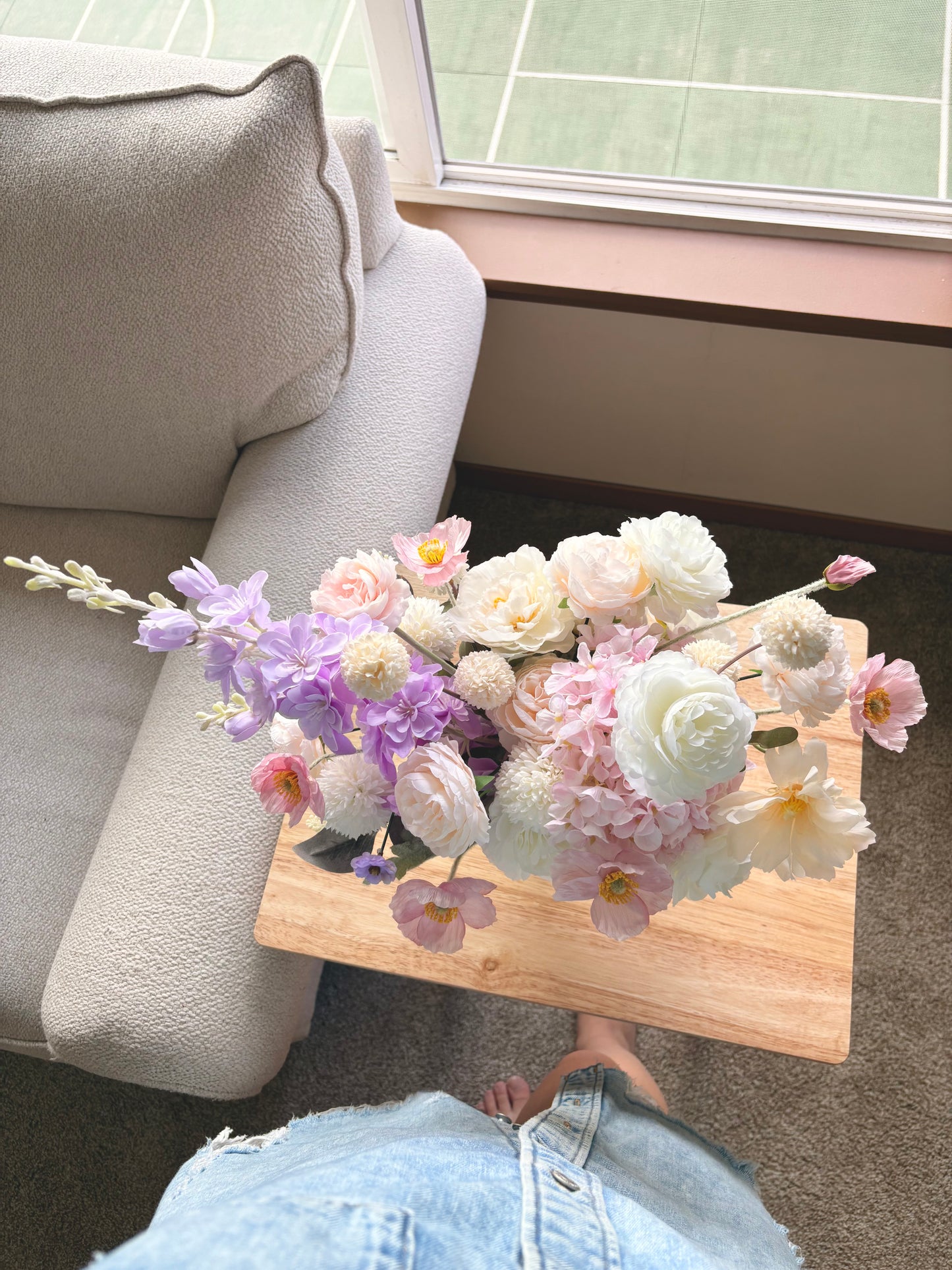 Bouquet of flowers on a wooden table next to a beige sofa.
