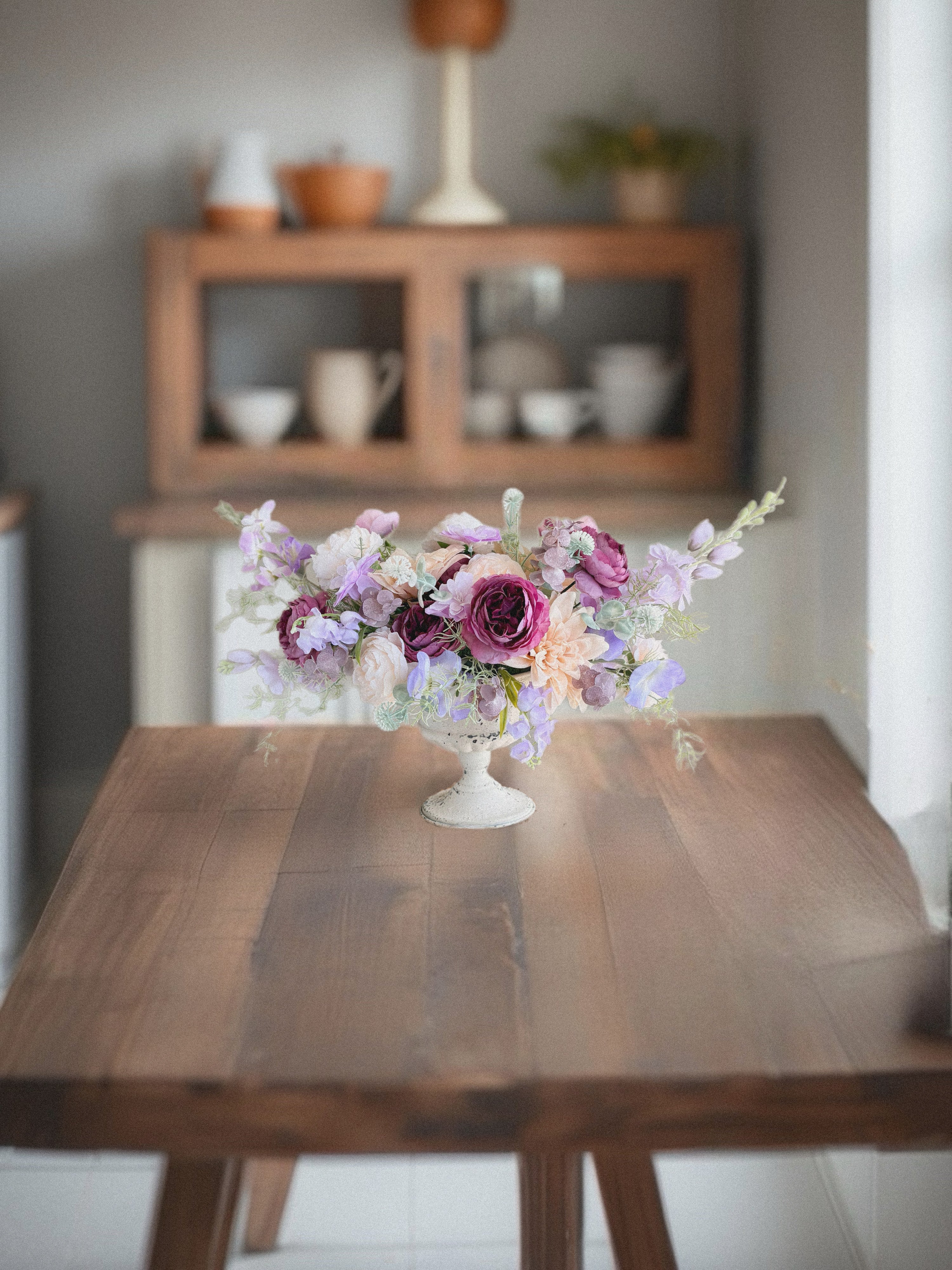 Floral arrangement in a white vase on a wooden table with a blurred background