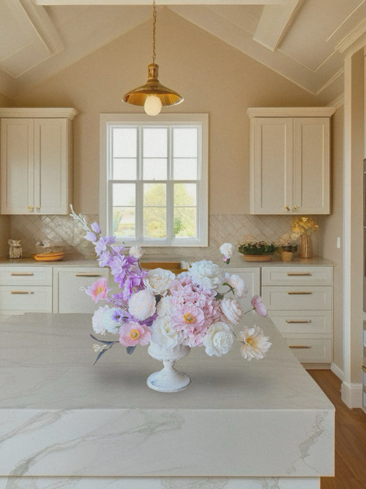 Floral arrangement on a kitchen counter with light-colored cabinets and a window in the background.