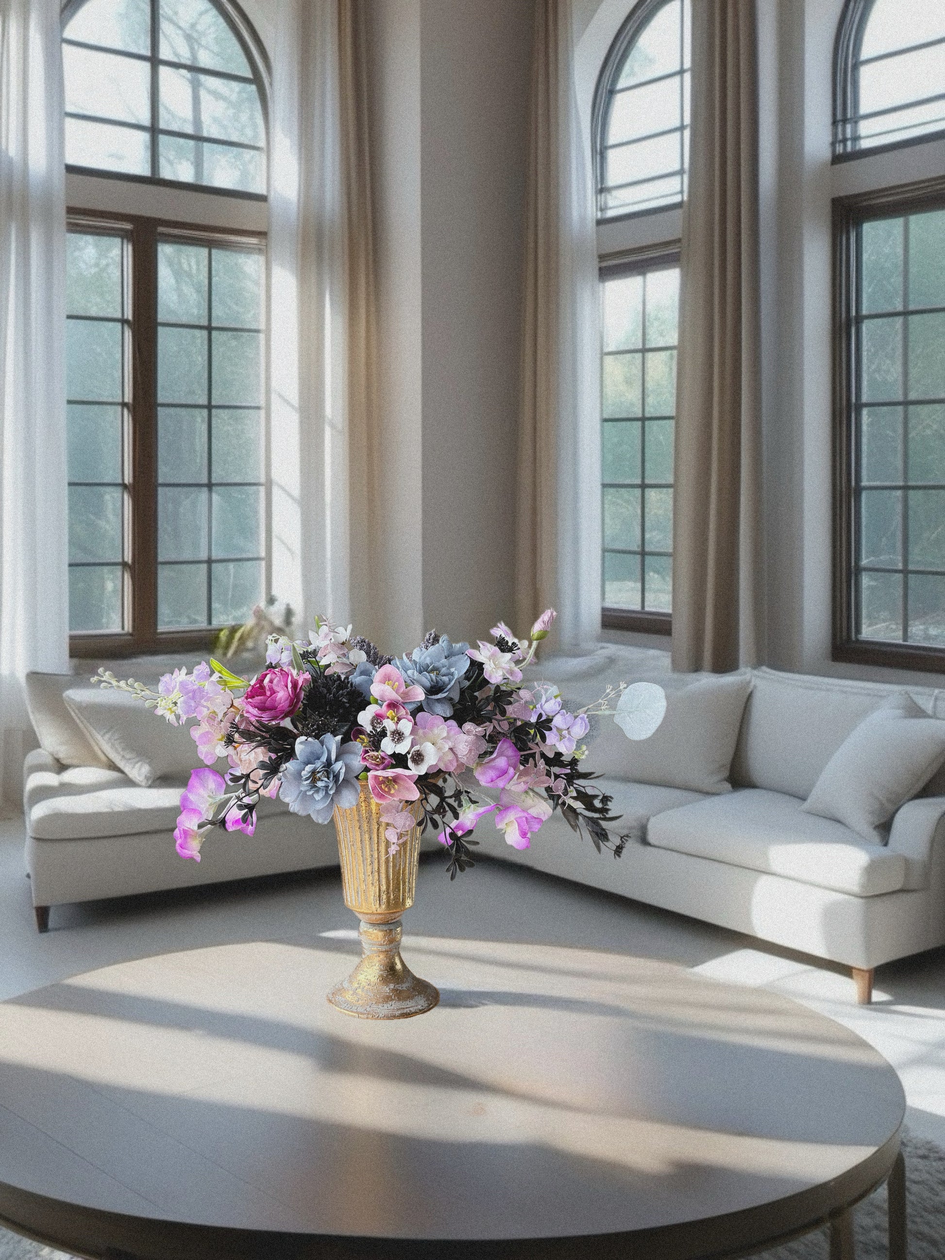 Living room with a round coffee table, floral arrangement, and large windows.