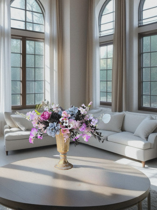 Living room with a round coffee table, floral arrangement, and large windows.
