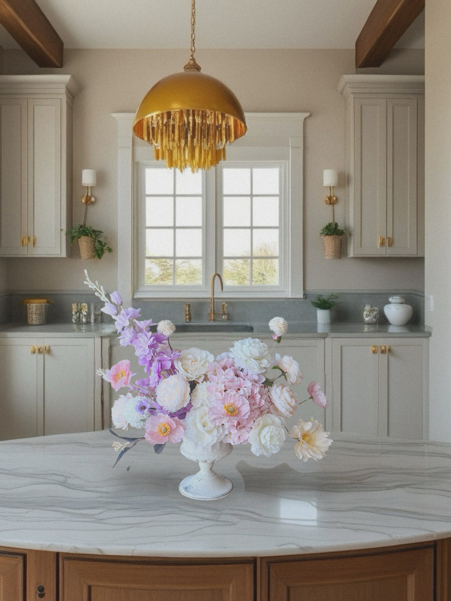 Kitchen with a floral arrangement on a marble countertop, gold pendant light, and white cabinets.