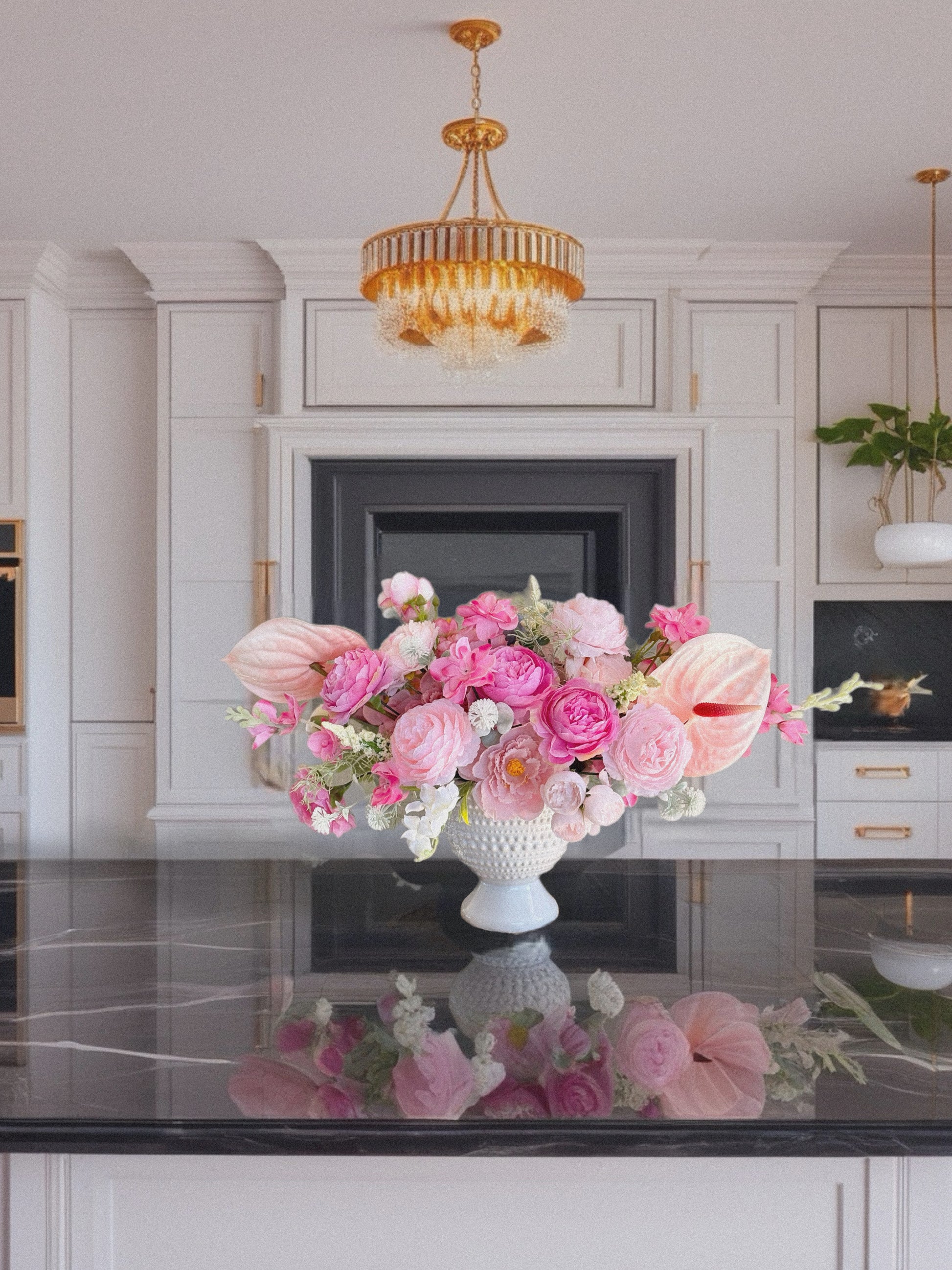 Floral arrangement in a white vase on a kitchen counter with a chandelier above.