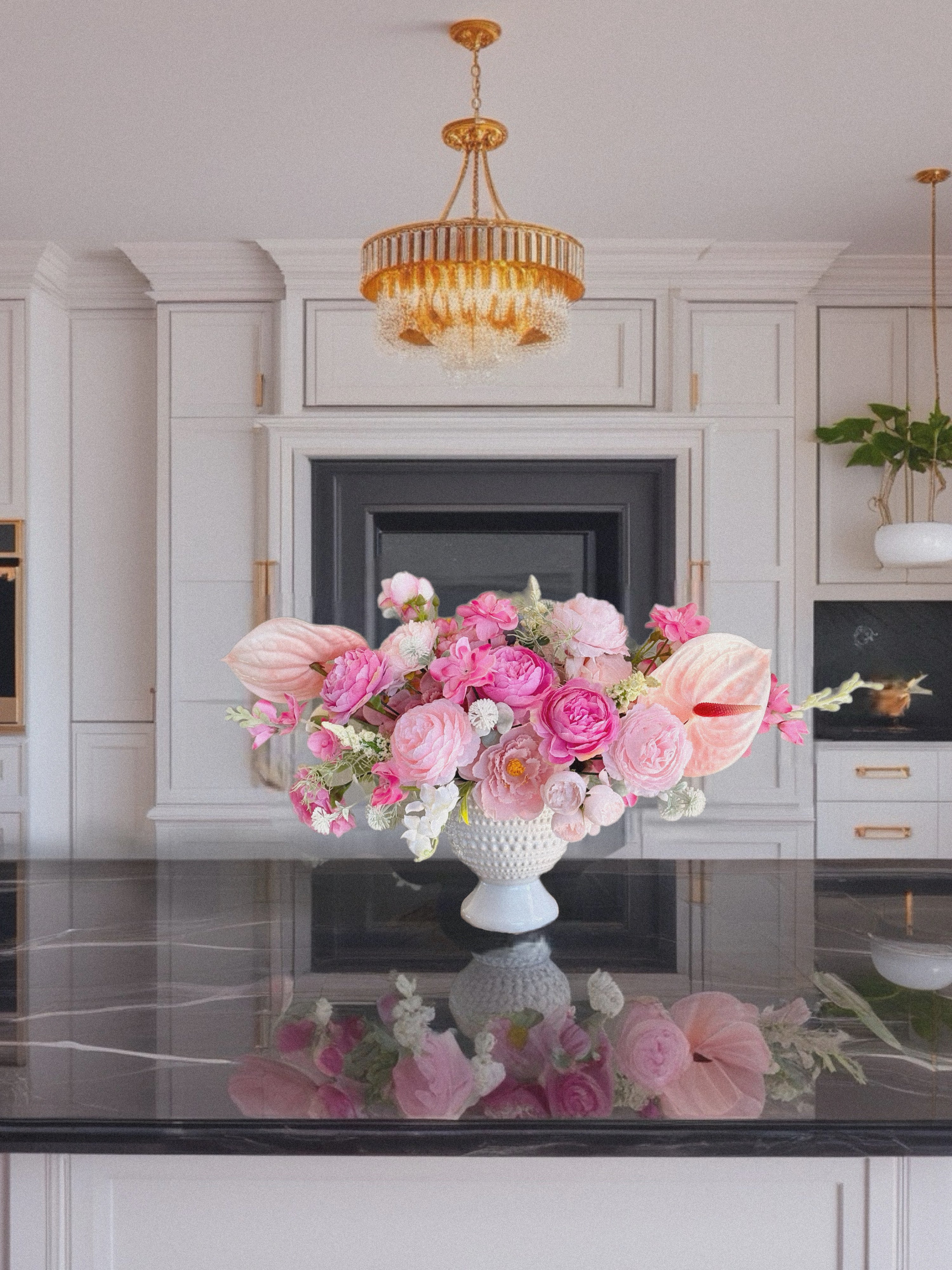 Floral arrangement in a white vase on a kitchen counter with a chandelier above.