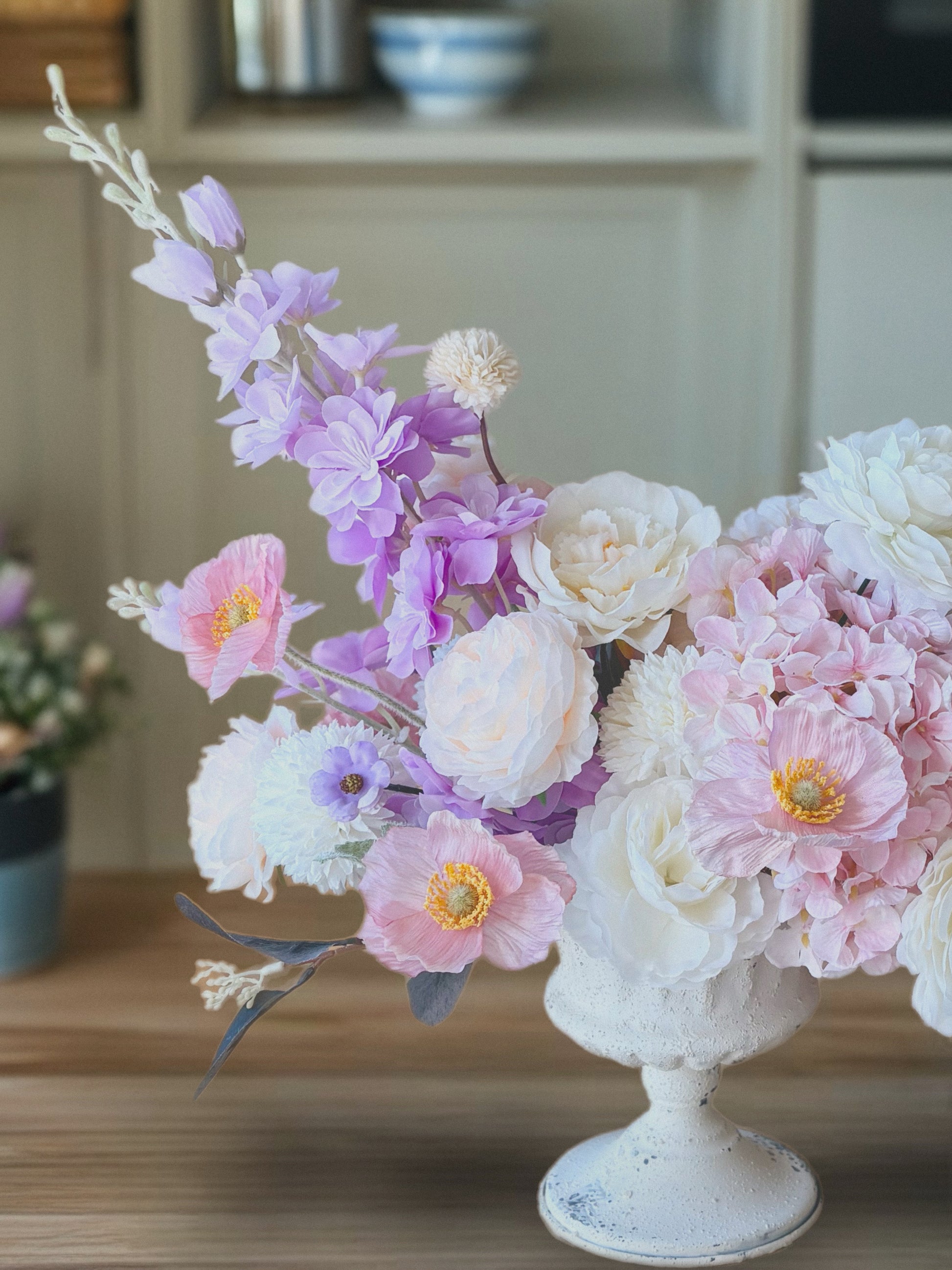 Floral arrangement in a white vase on a wooden surface with a blurred background