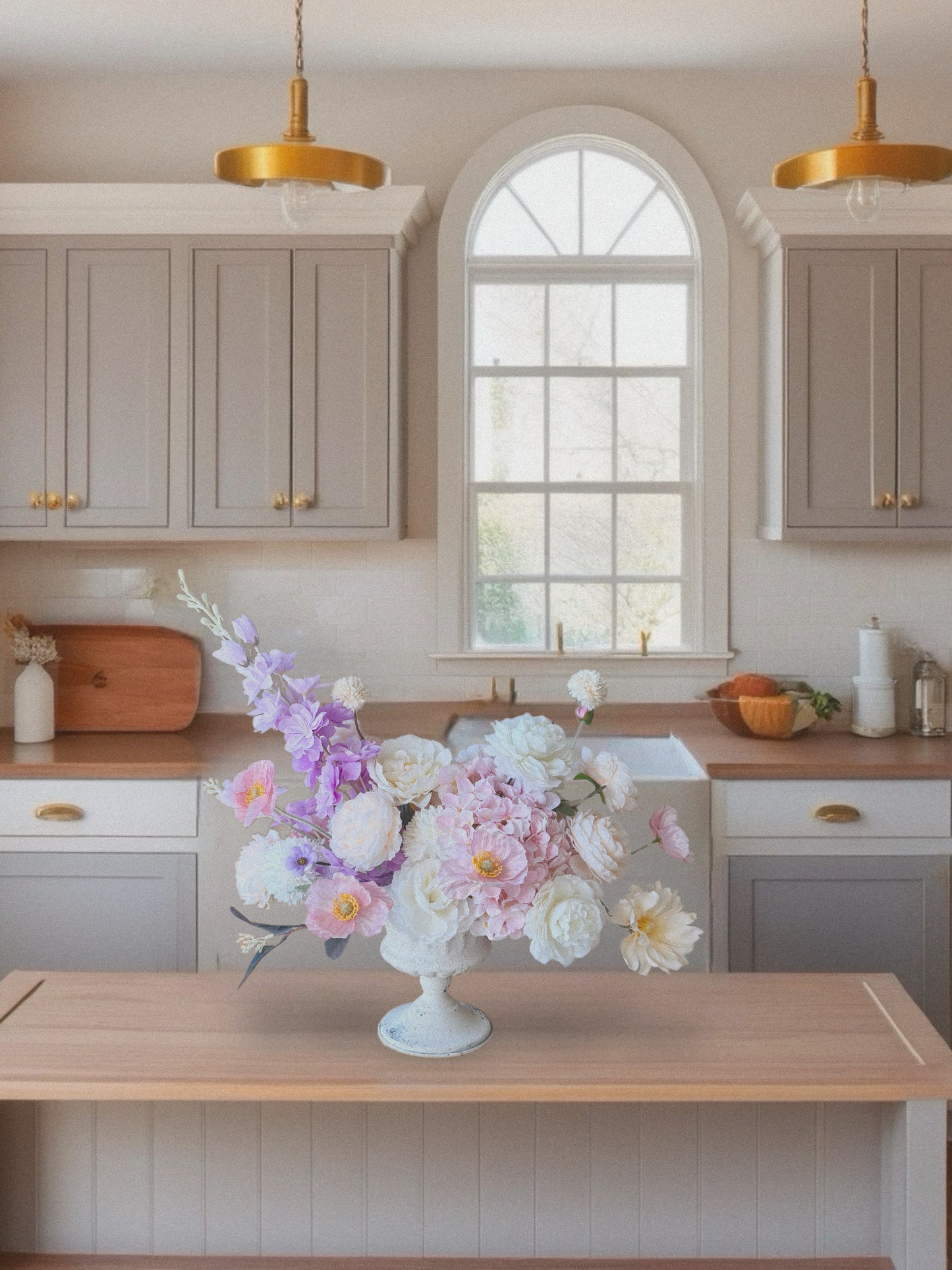 Kitchen with light gray cabinets, wooden countertops, and a vase of flowers on a table.