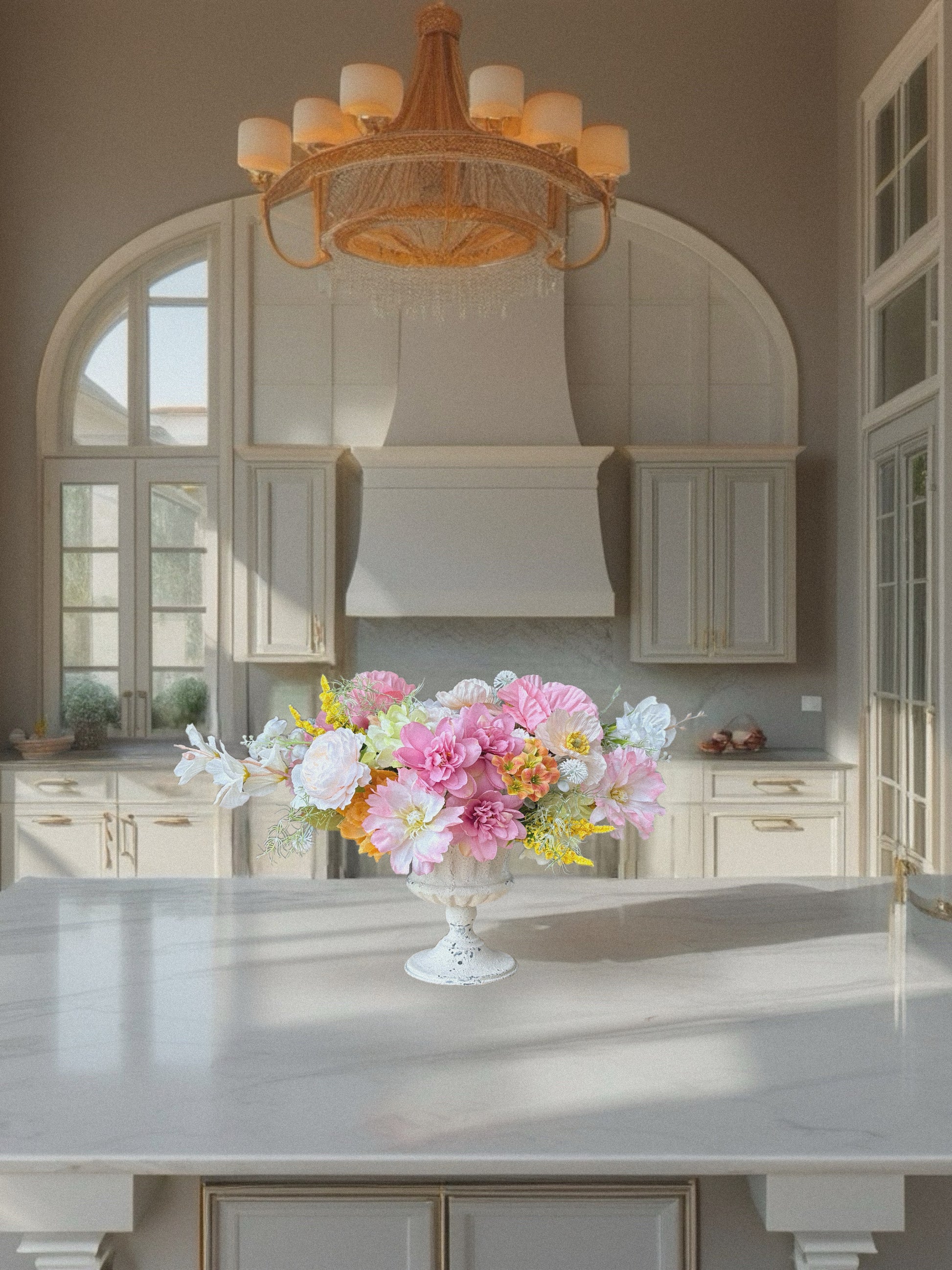 Kitchen with a floral arrangement on a counter, elegant chandelier, and large windows.