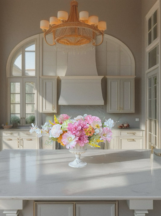 Kitchen with a floral arrangement on a counter, elegant chandelier, and large windows.