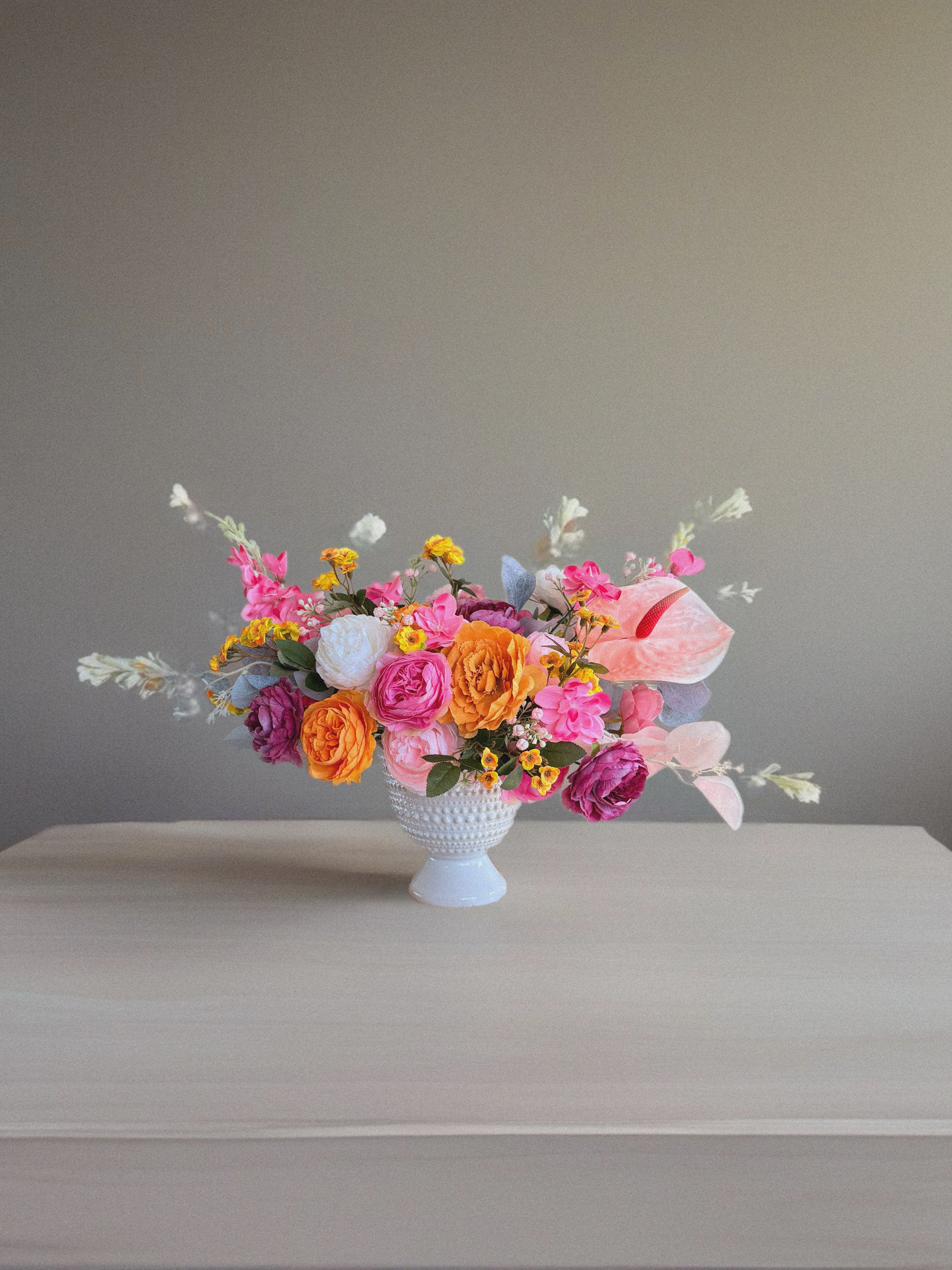 Colorful flower arrangement in a white vase on a gray surface with a neutral background
