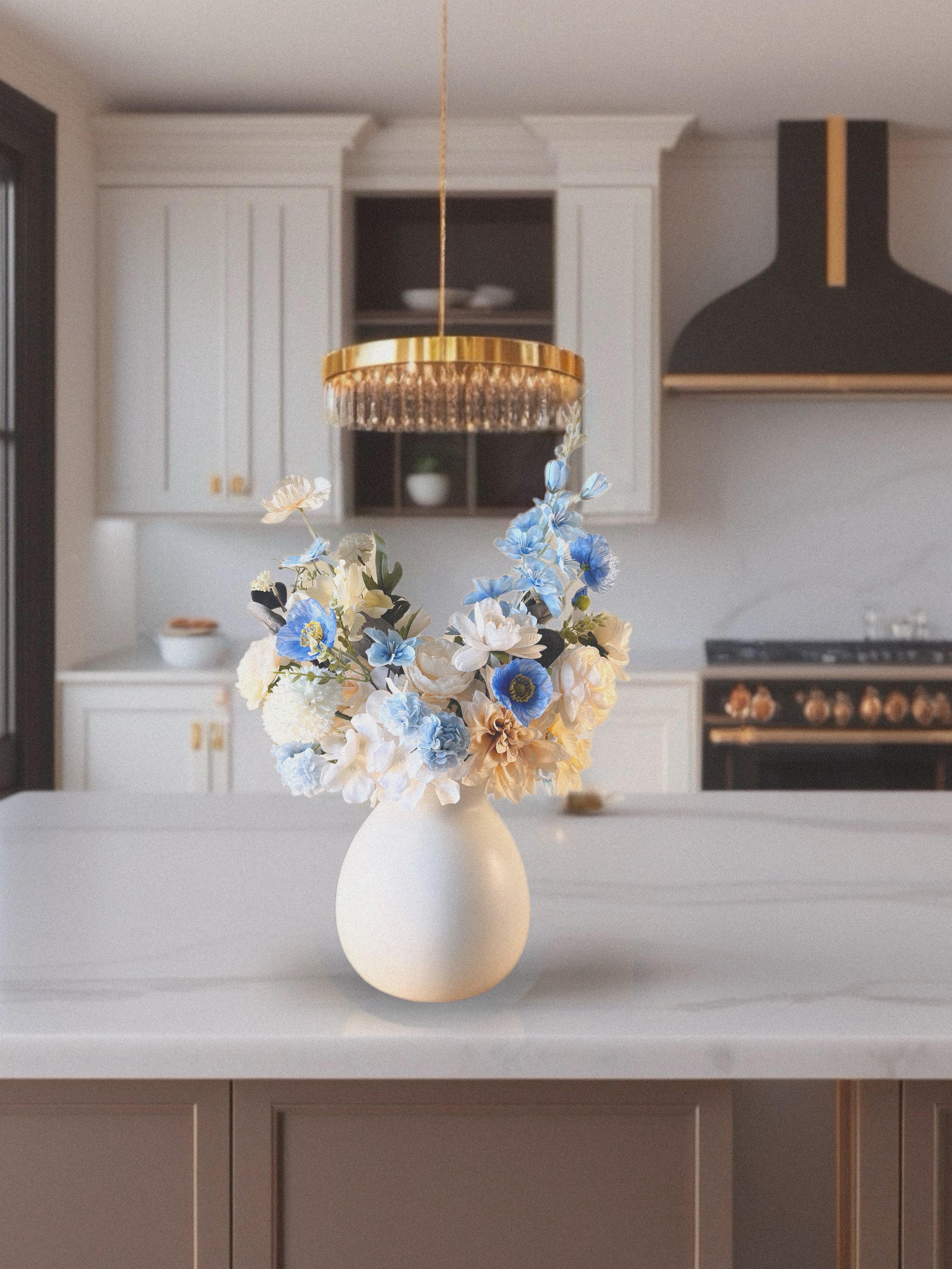 Decorative flowers in a white vase on a kitchen counter with a modern chandelier above.