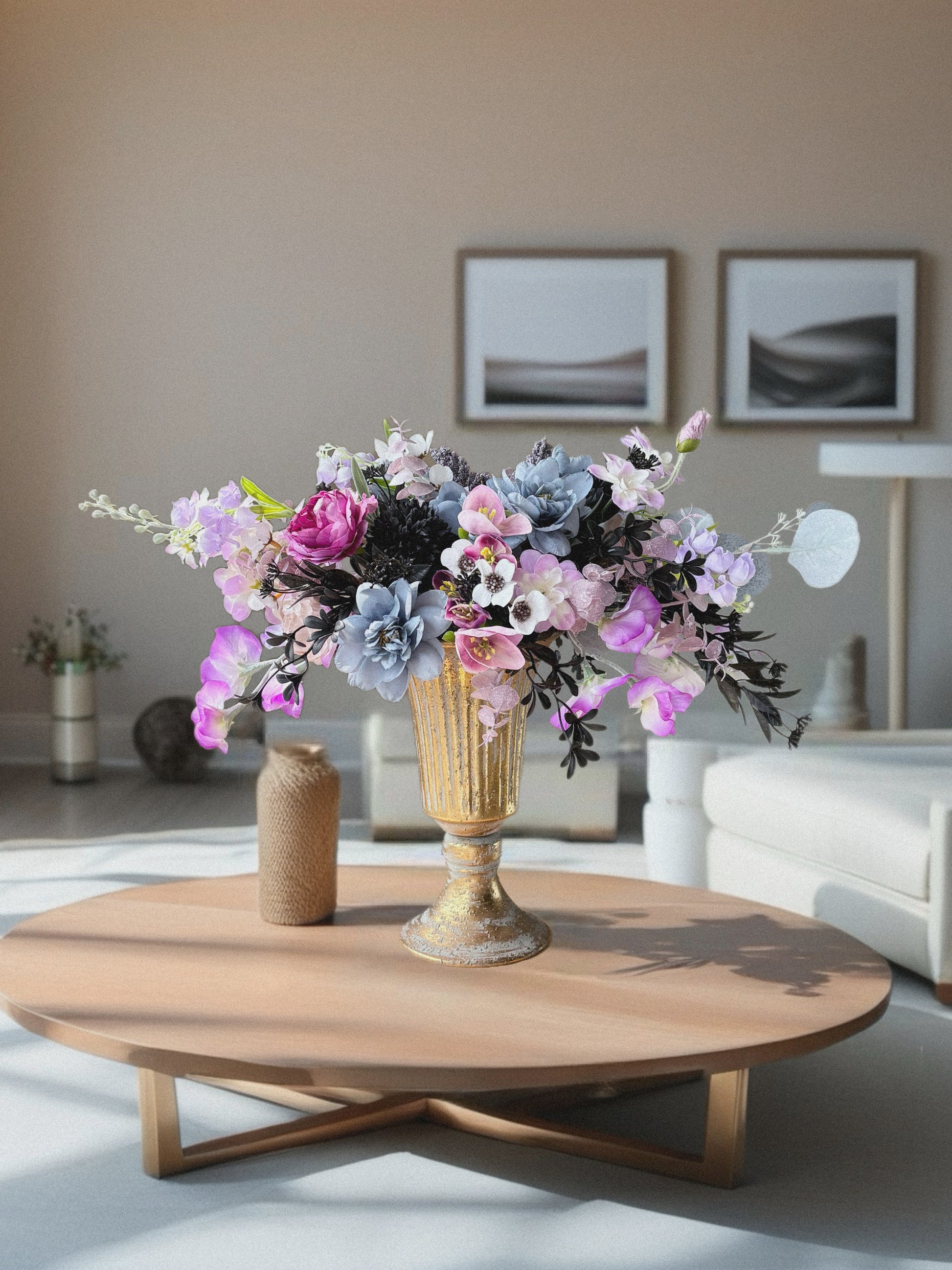 Floral arrangement in a gold vase on a wooden coffee table in a living room.