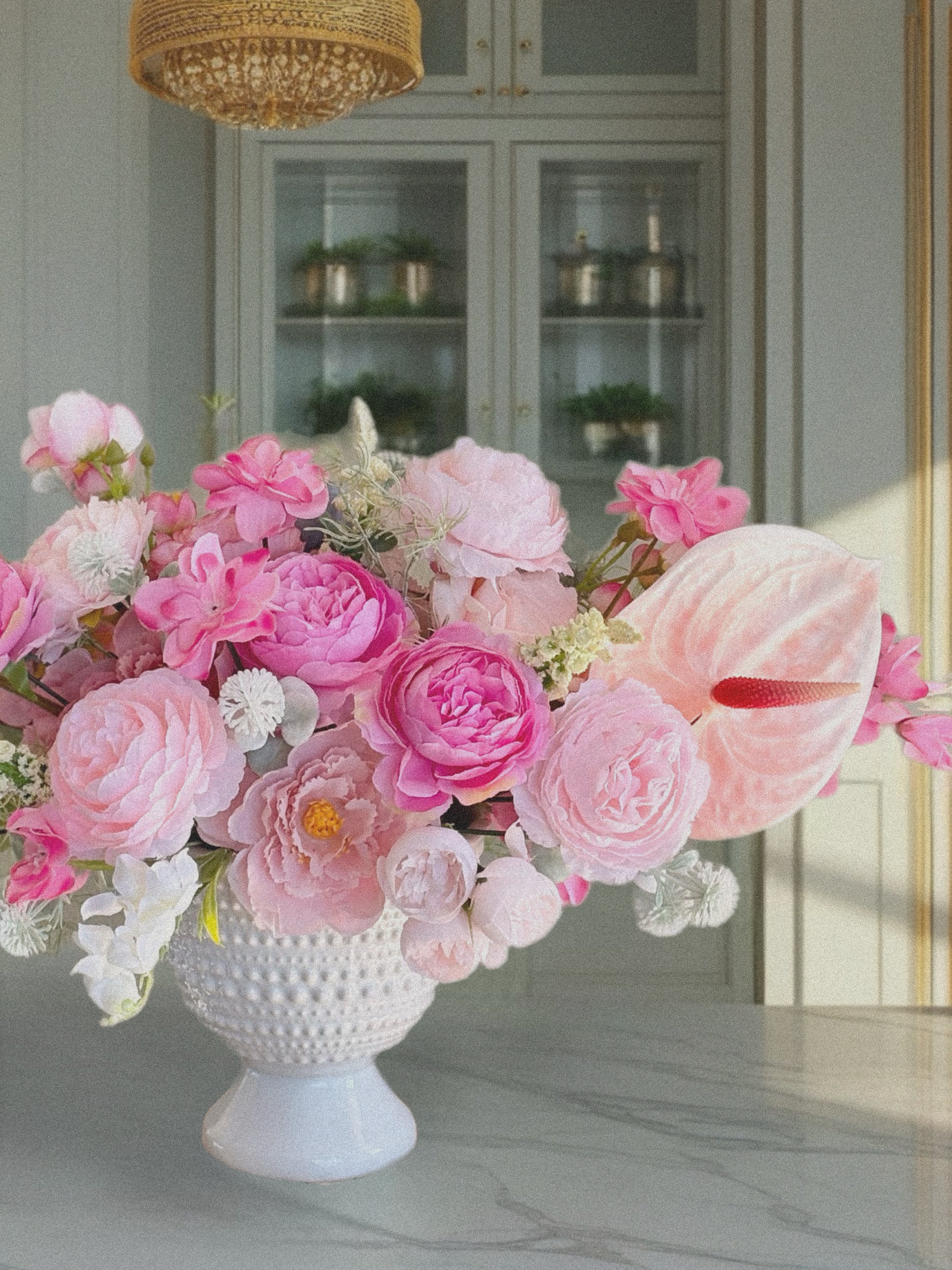 Bouquet of pink and white flowers in a textured white vase on a marble surface.