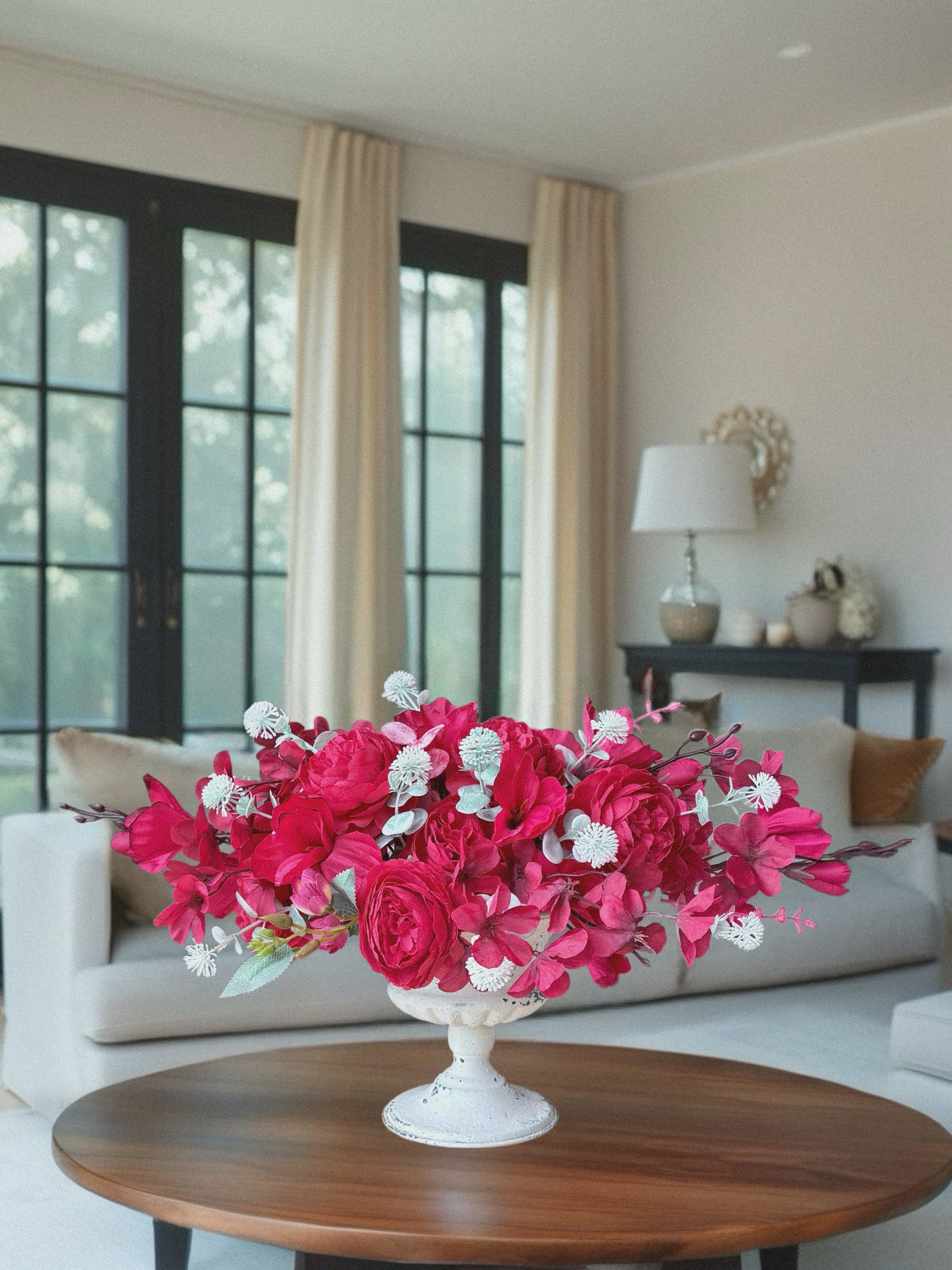 Floral arrangement in a white vase on a wooden table in a living room.