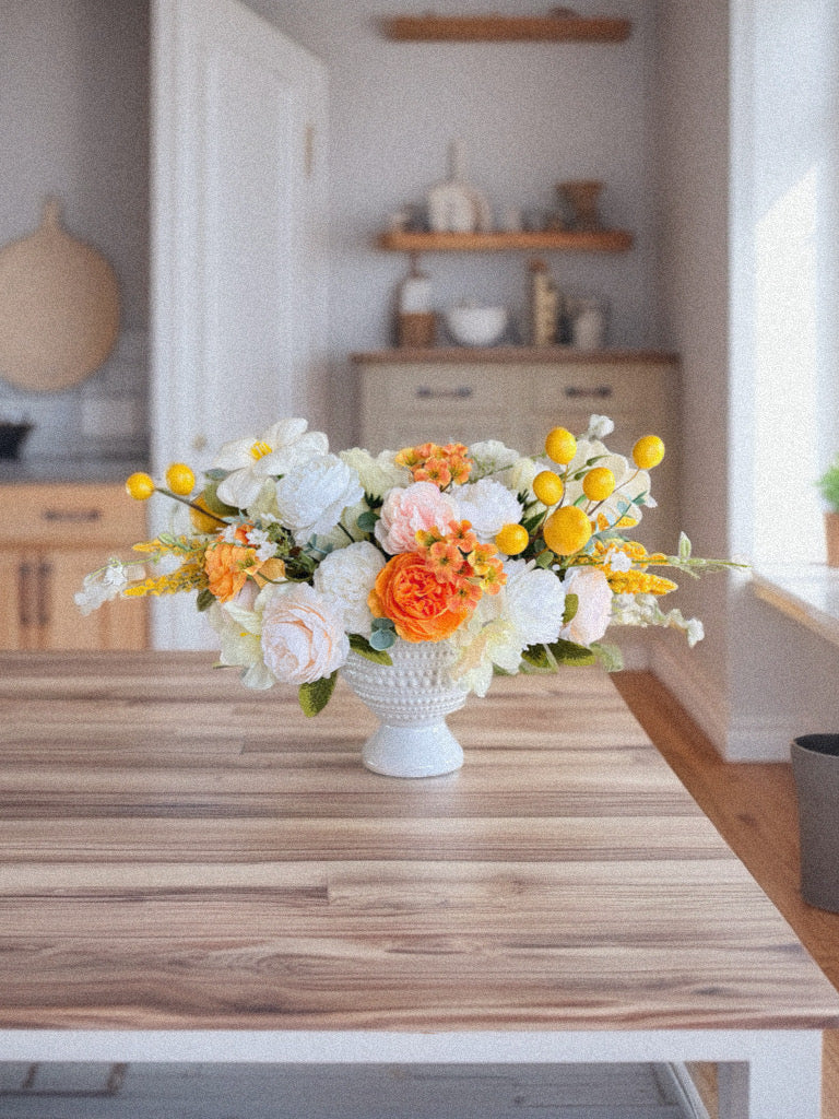 Floral arrangement in a white vase on a wooden table in a kitchen.