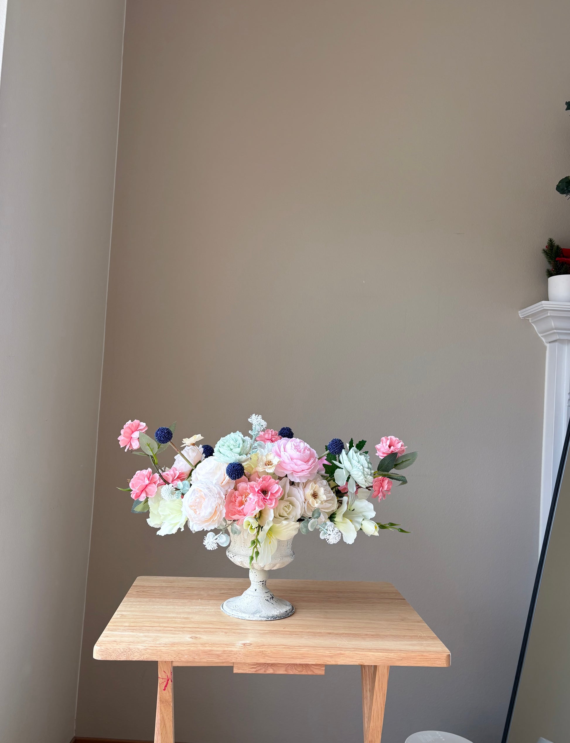 Floral arrangement in a white vase on a wooden table against a plain wall.