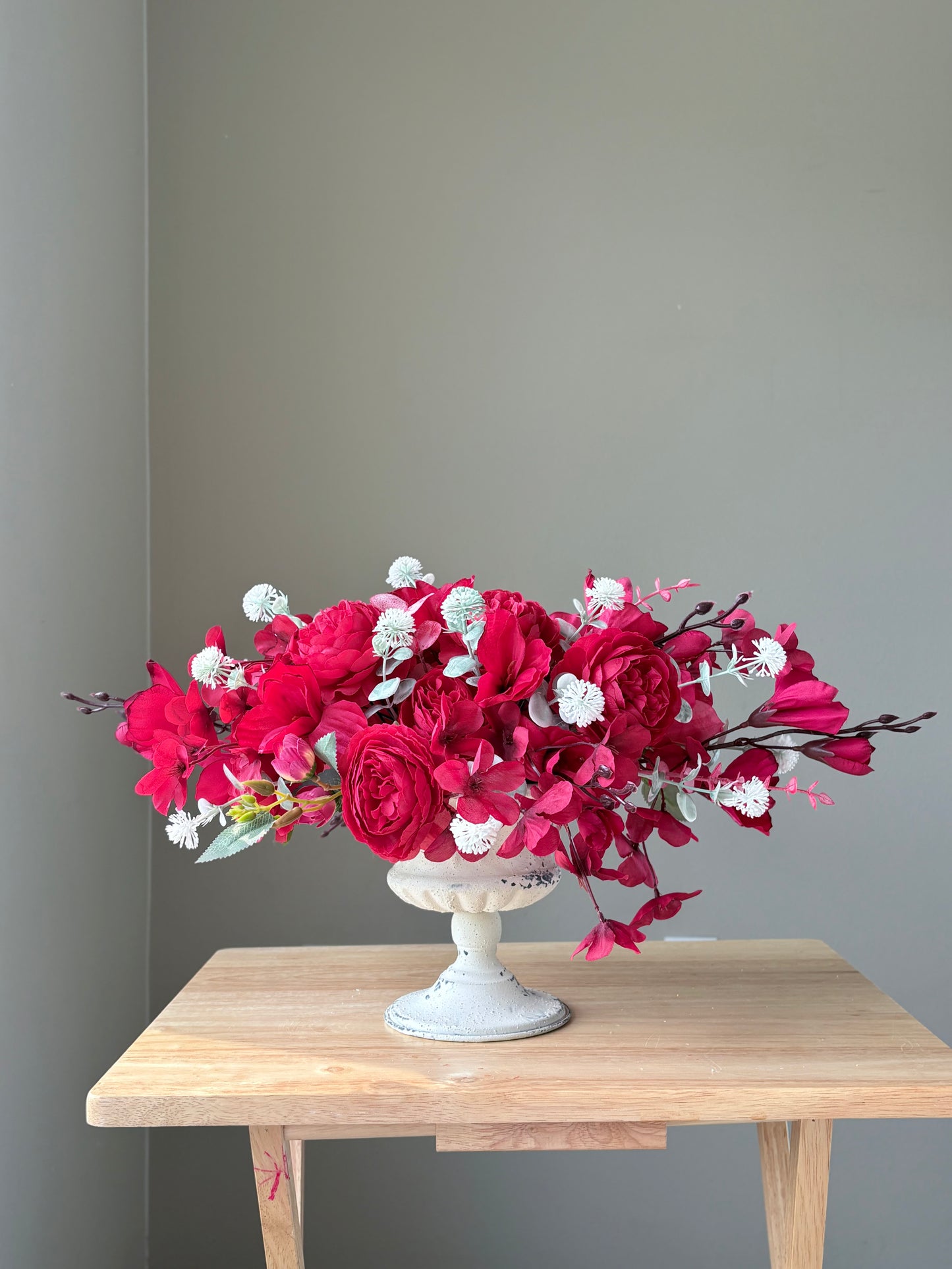 Bouquet of red and white flowers in a white vase on a wooden table against a gray wall.