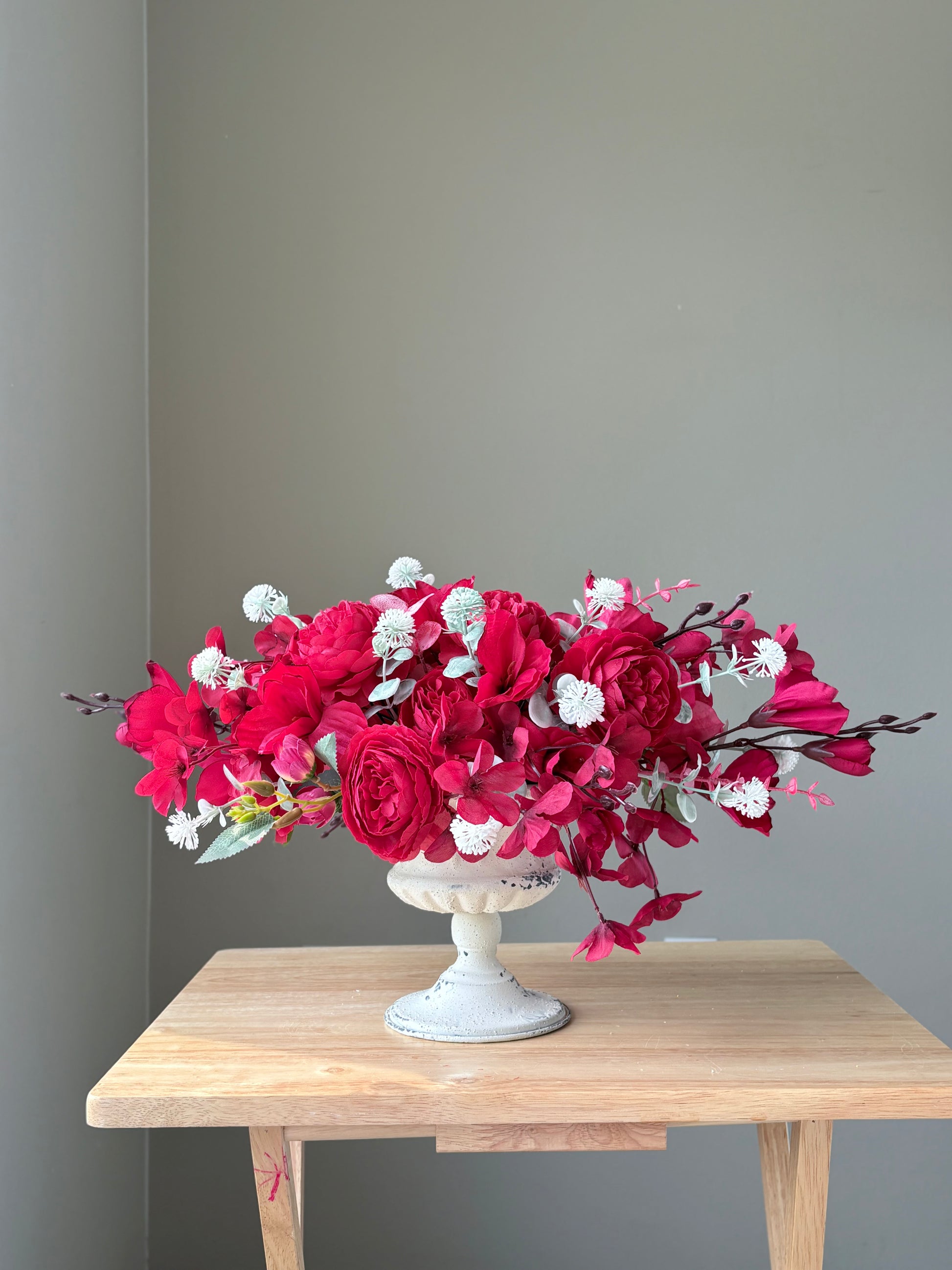 Bouquet of red and white flowers in a white vase on a wooden table against a gray wall.