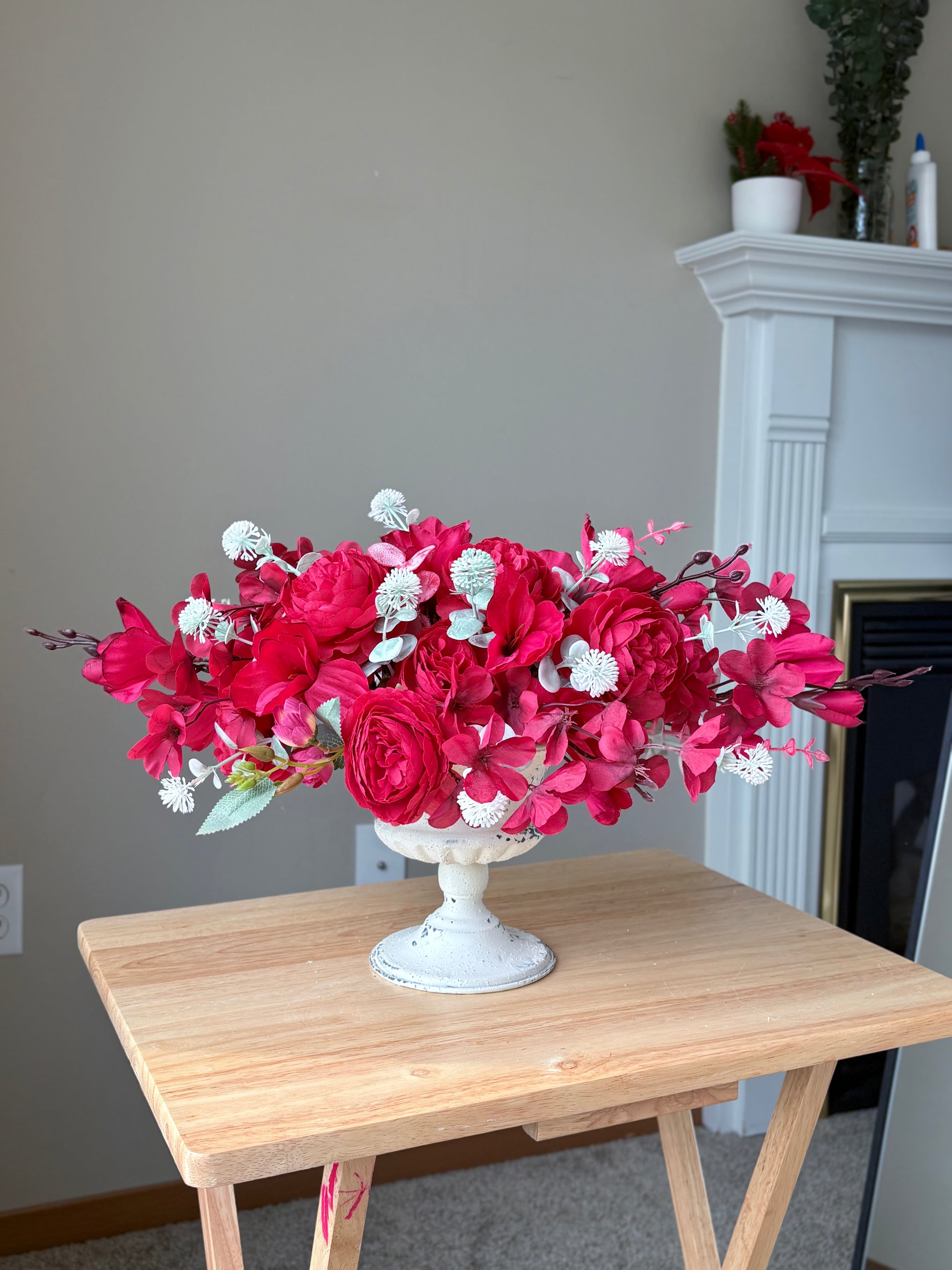 Bouquet of red and white flowers in a white vase on a wooden table.