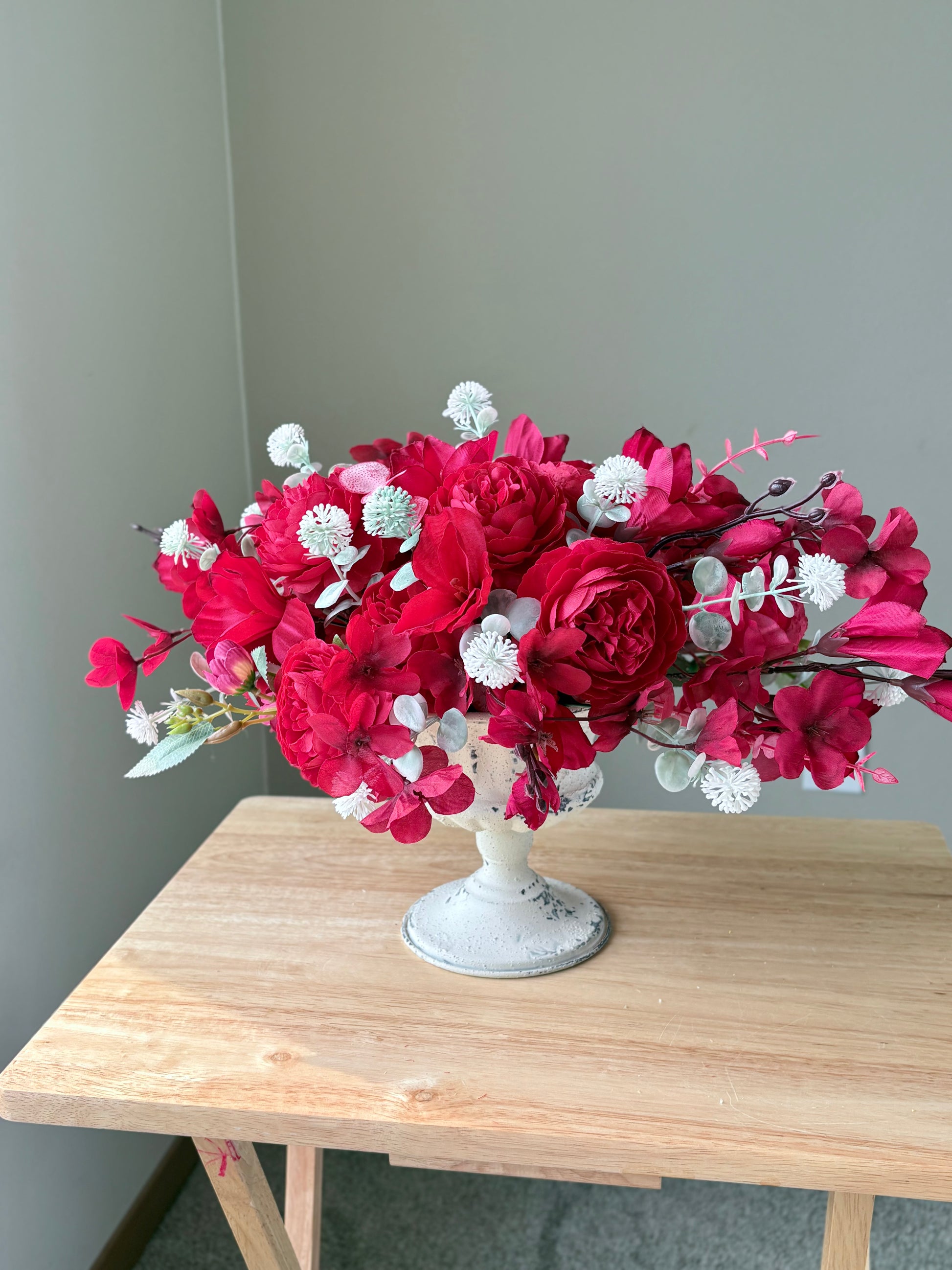 Bouquet of red flowers in a white vase on a wooden table against a gray wall.