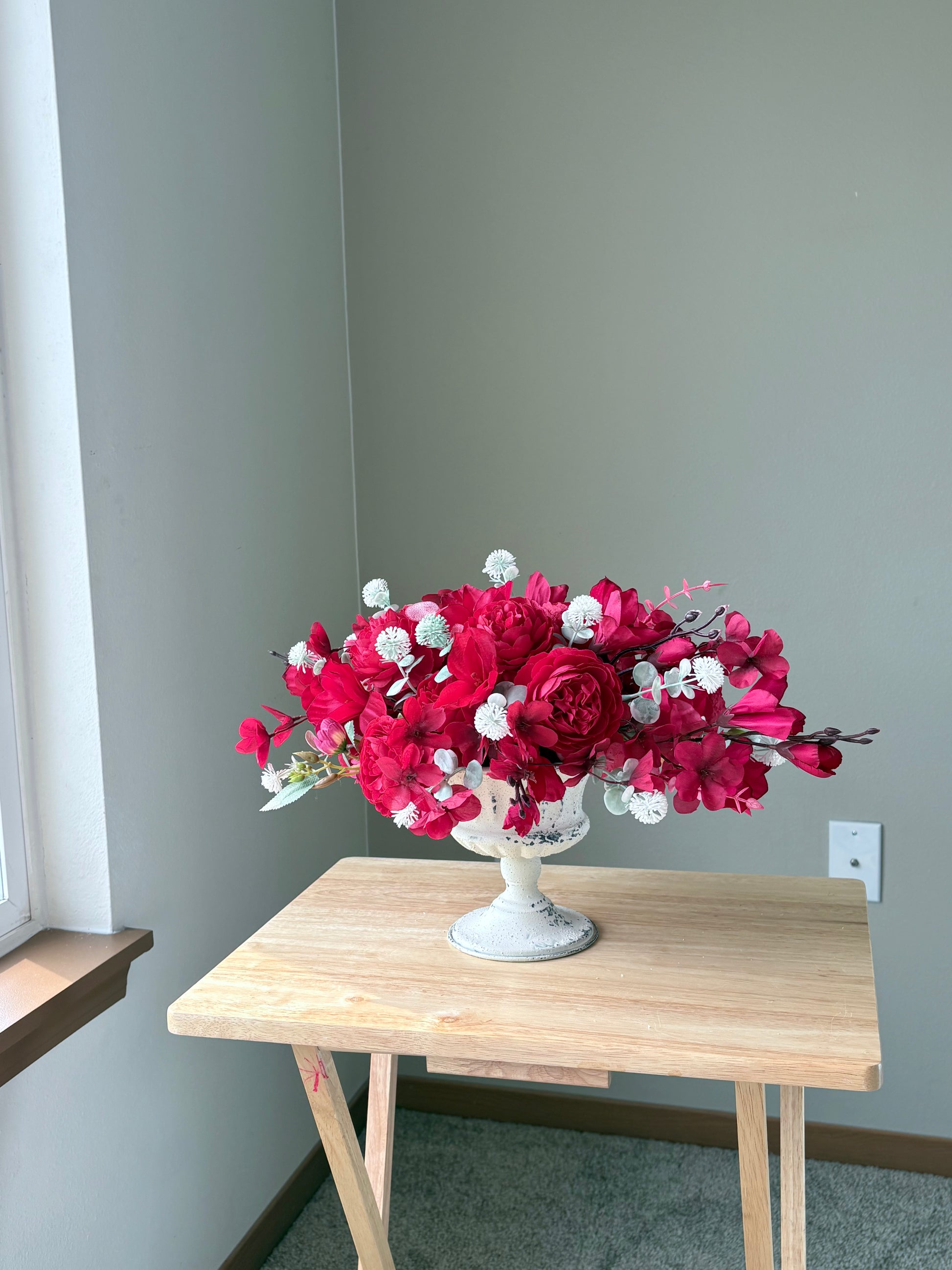 Bouquet of pink flowers in a white vase on a wooden table against a gray wall.