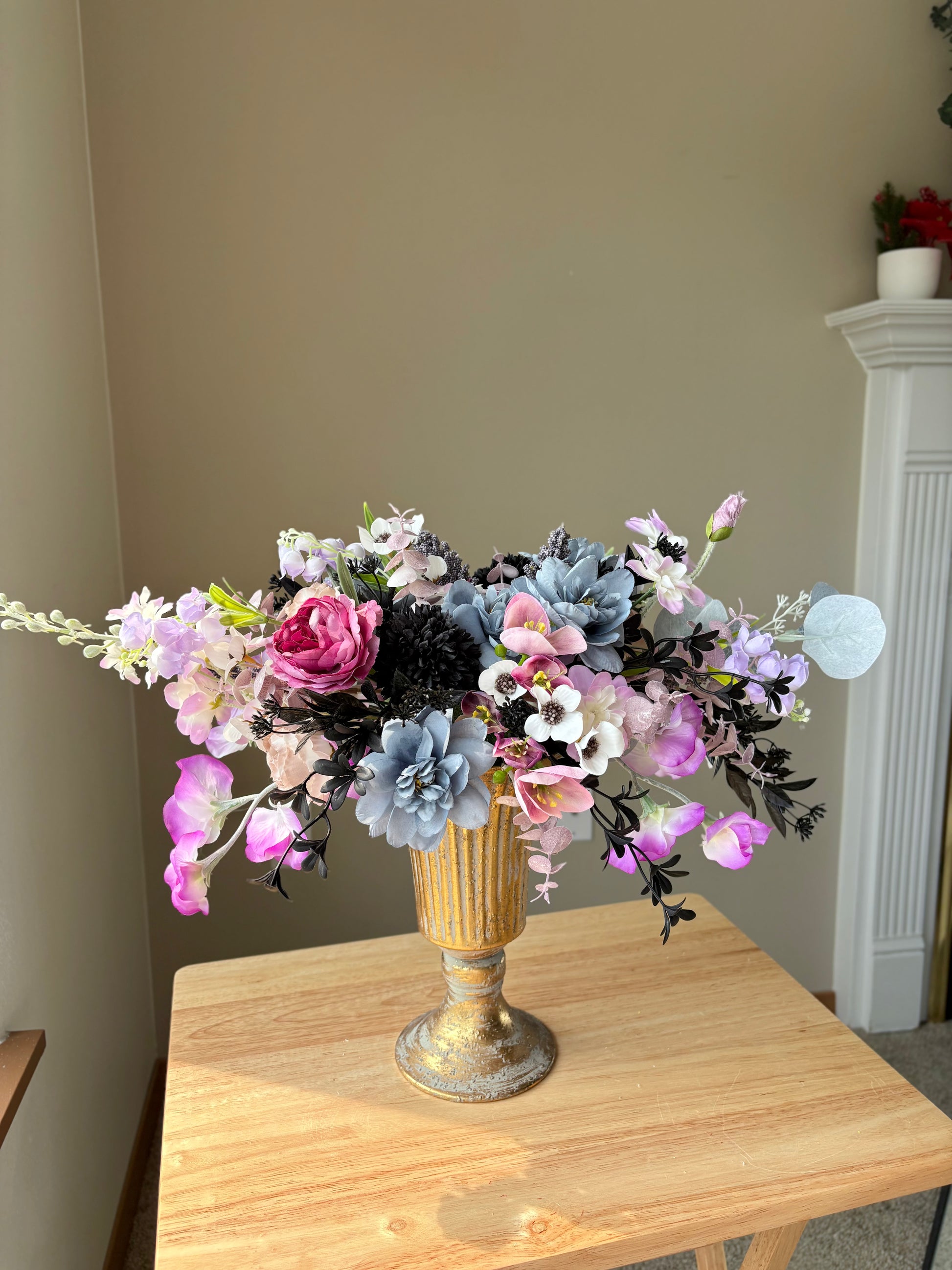 Bouquet of flowers in a gold vase on a wooden table against a neutral wall.