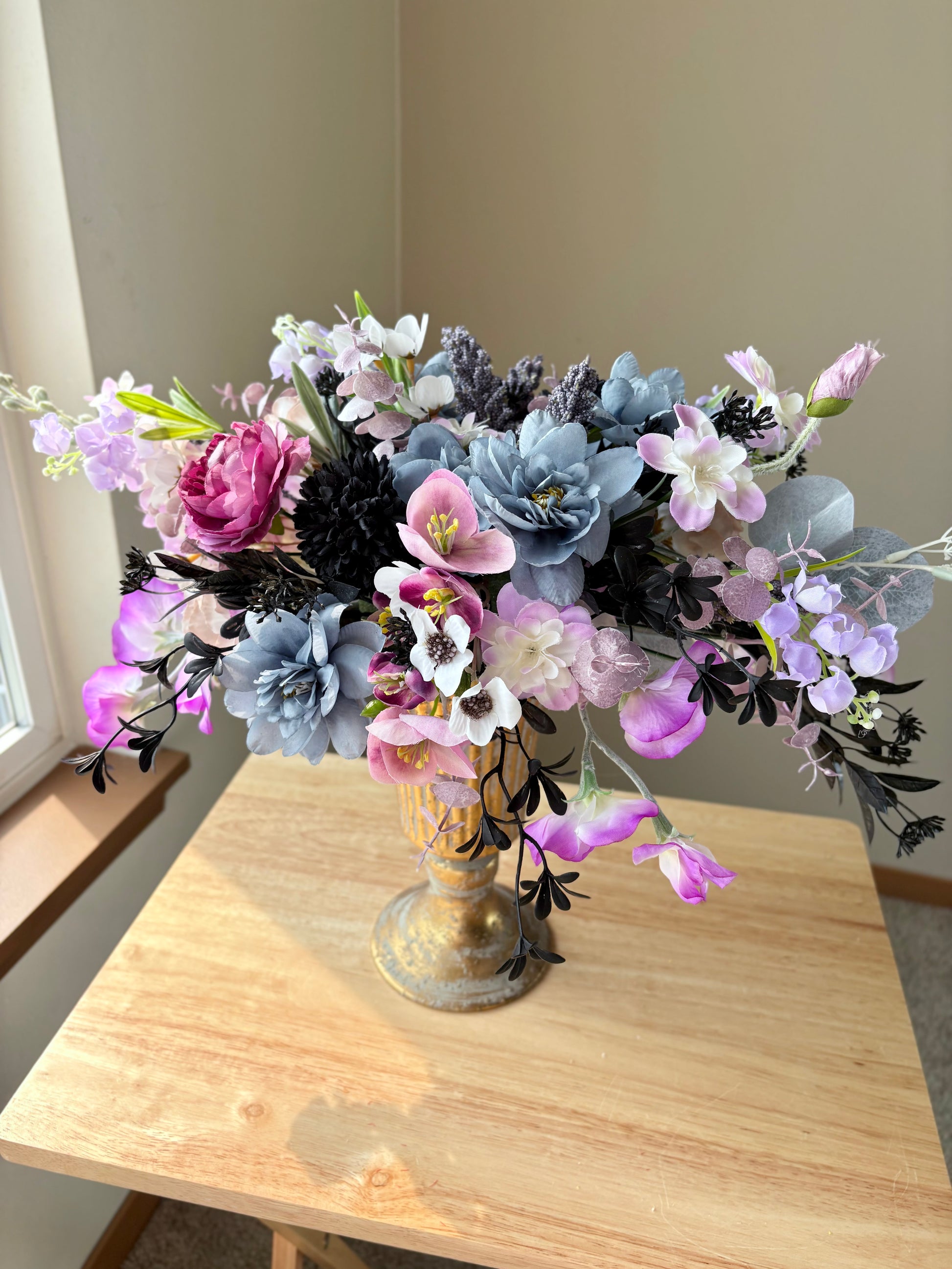 Bouquet of artificial flowers in a decorative vase on a wooden table.