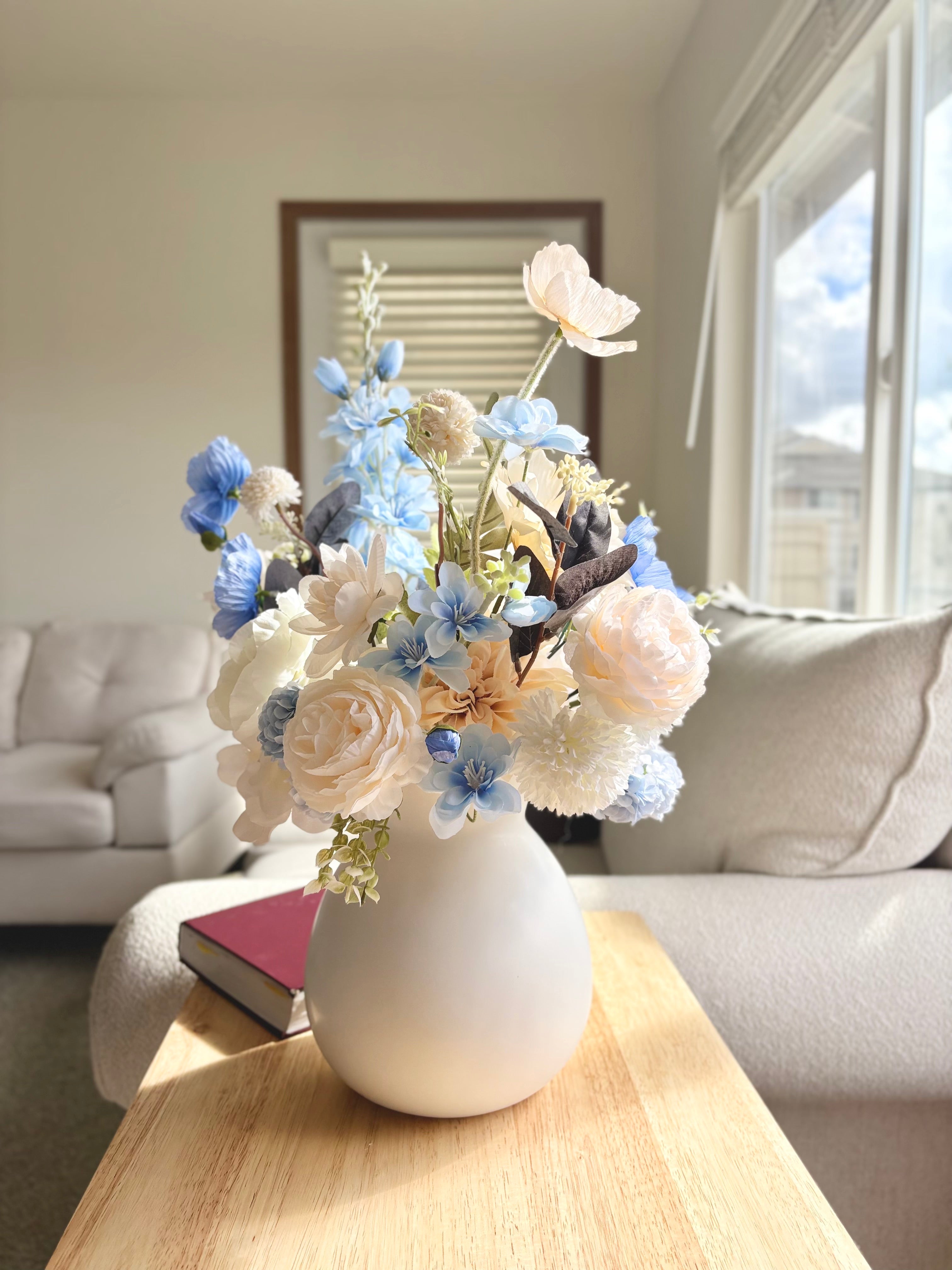 White vase with flowers on a wooden coffee table in a living room.