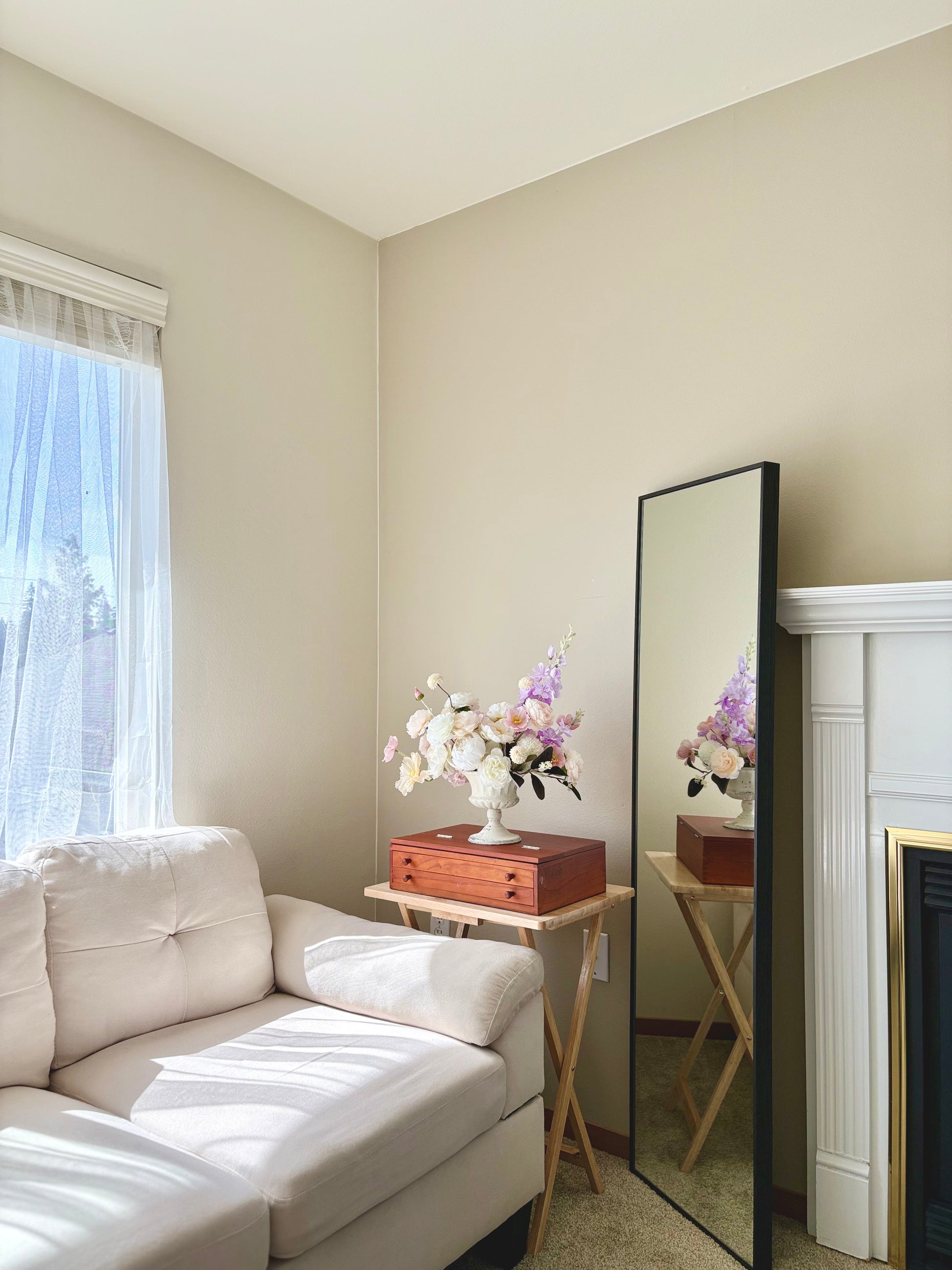 Living room with a white sofa, small table with flowers, and a full-length mirror.