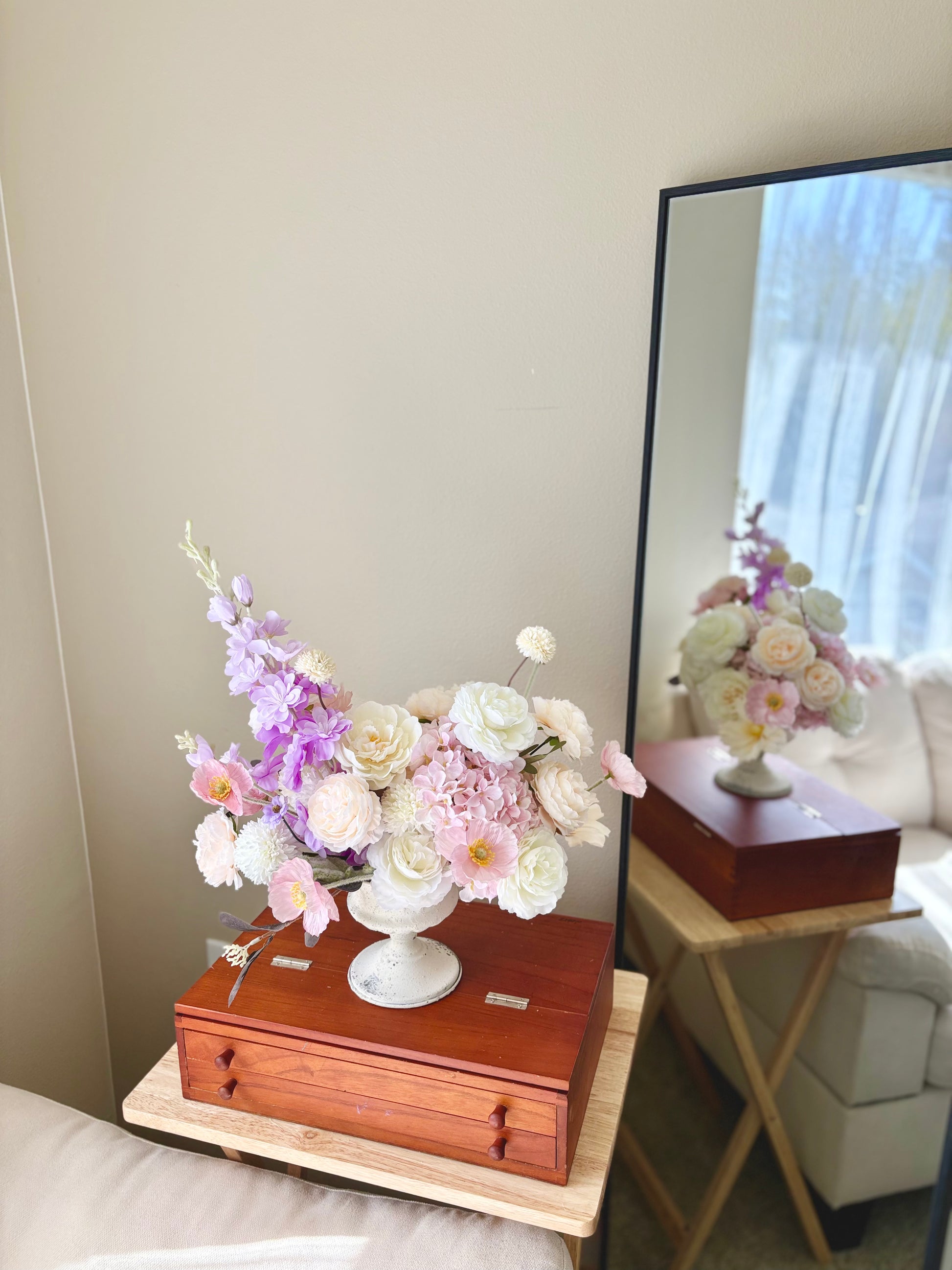 Floral arrangement on a wooden box with a mirror reflecting the scene.