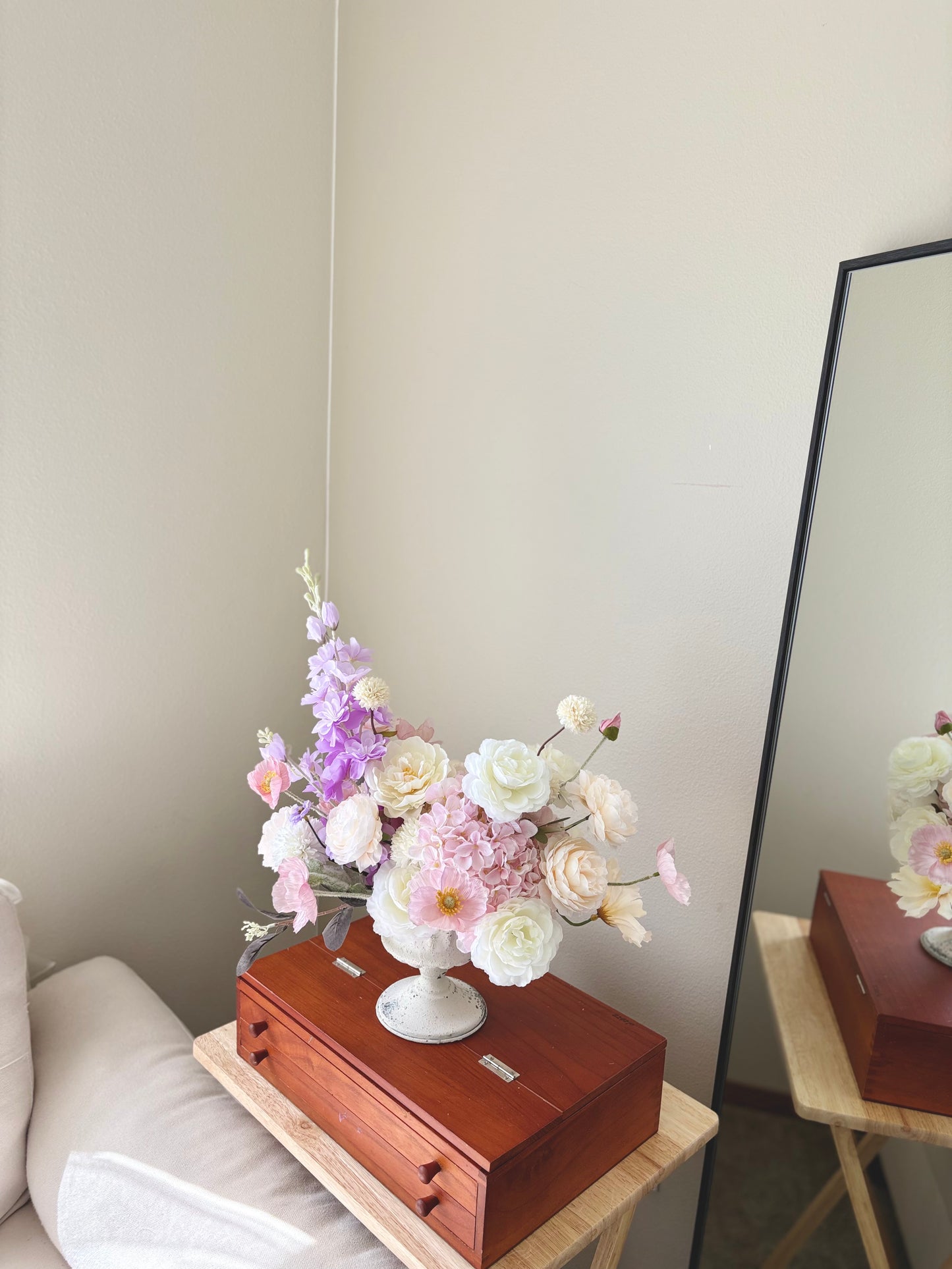 Floral arrangement in a white vase on a wooden box with a mirror in the background.