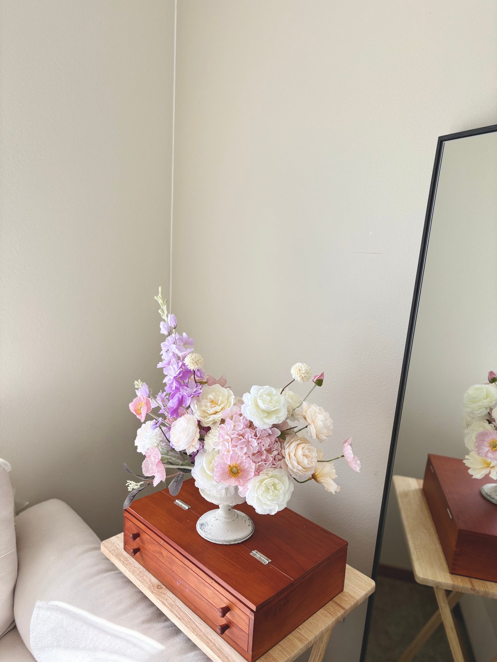 Floral arrangement in a white vase on a wooden box with a mirror in the background.