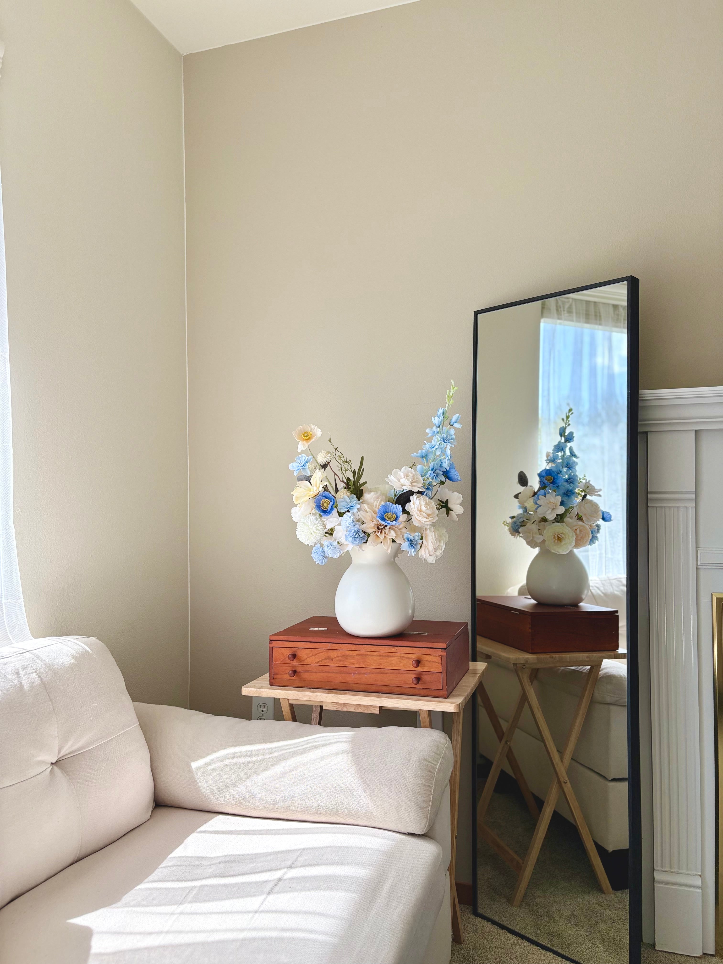 Room interior with a vase of flowers on a table, a mirror reflecting the room, and a white sofa.
