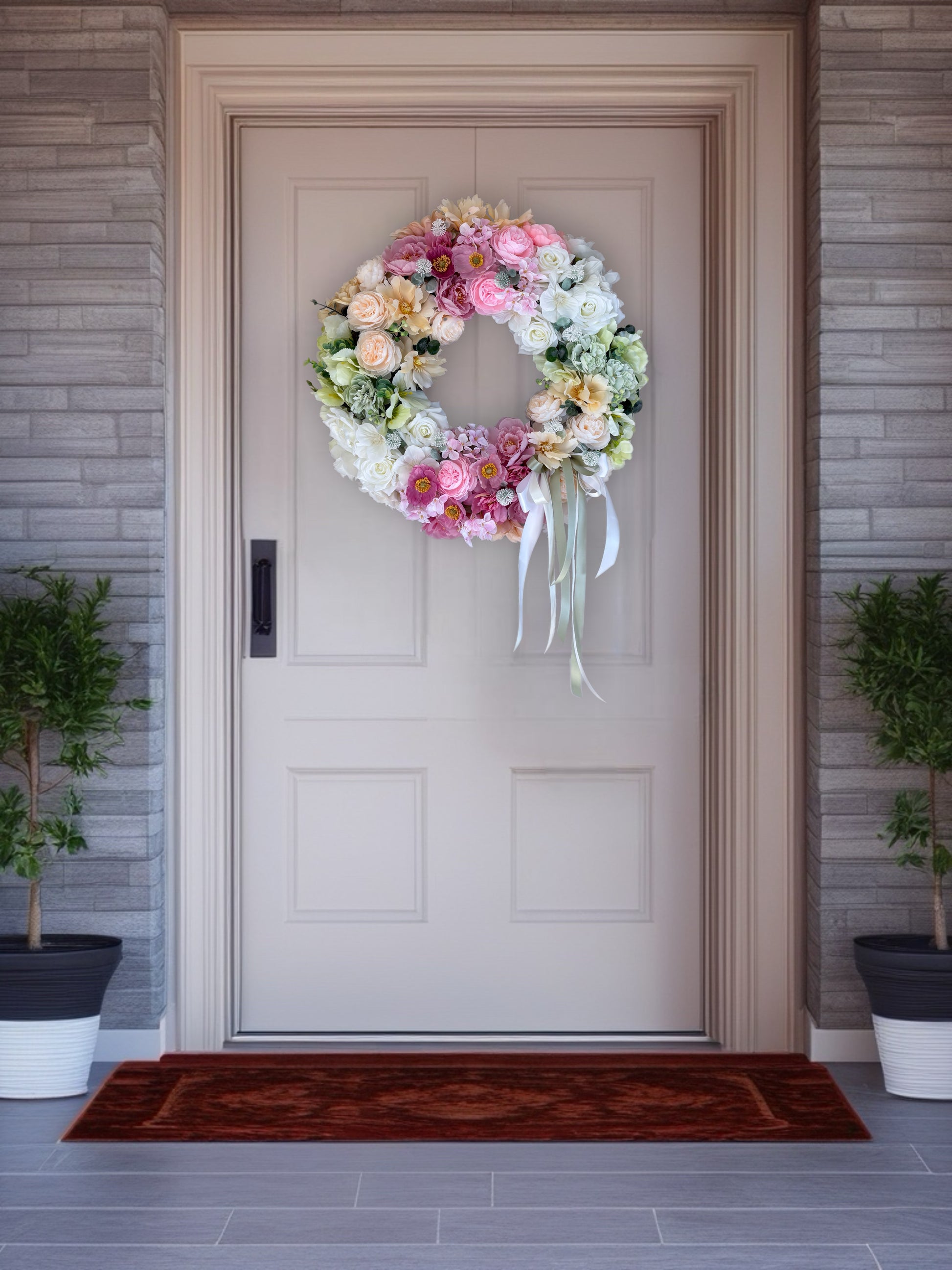 Floral wreath on a door with a doormat and plants.