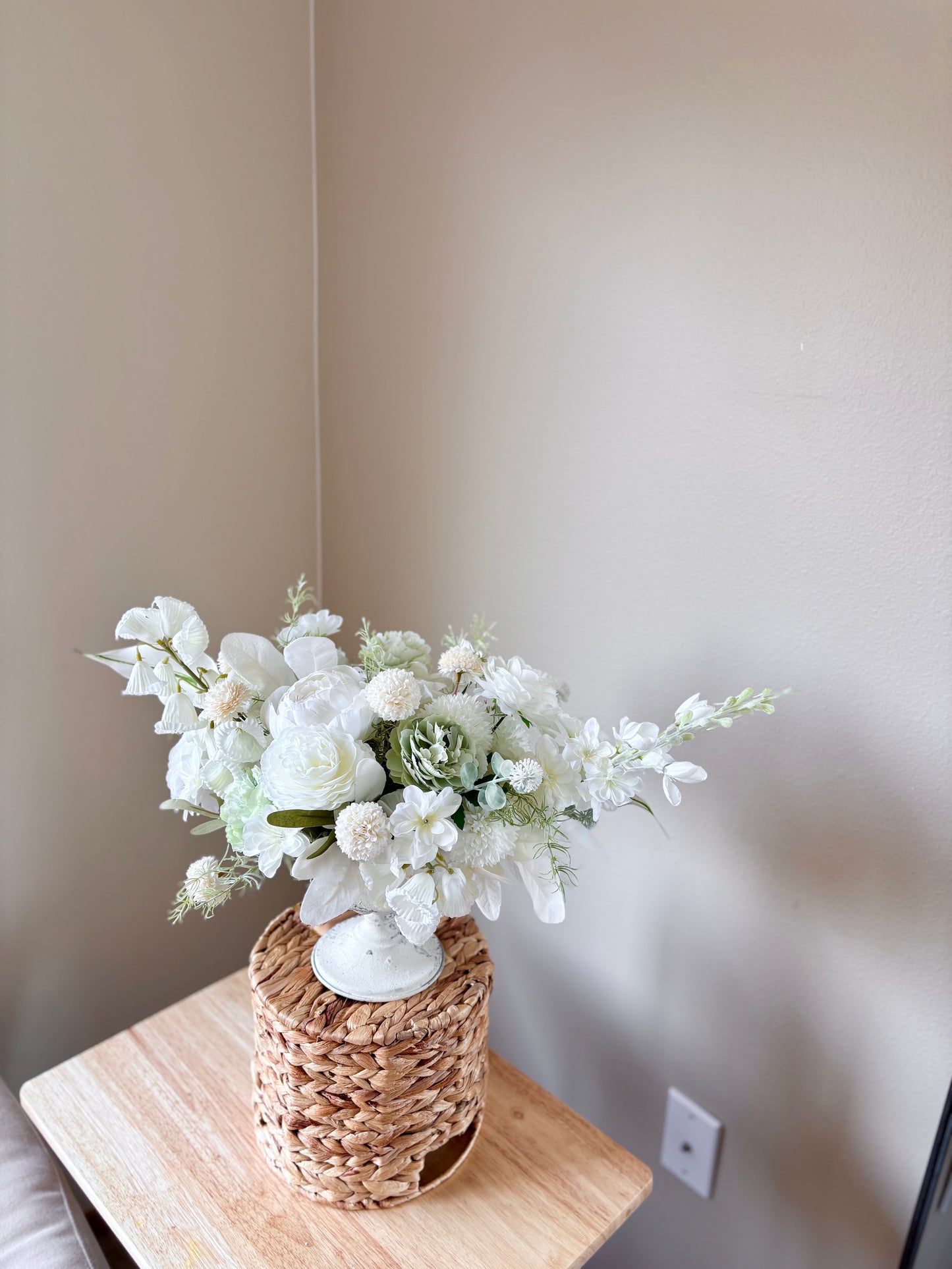 Floral arrangement in a woven basket on a wooden surface with a neutral wall background