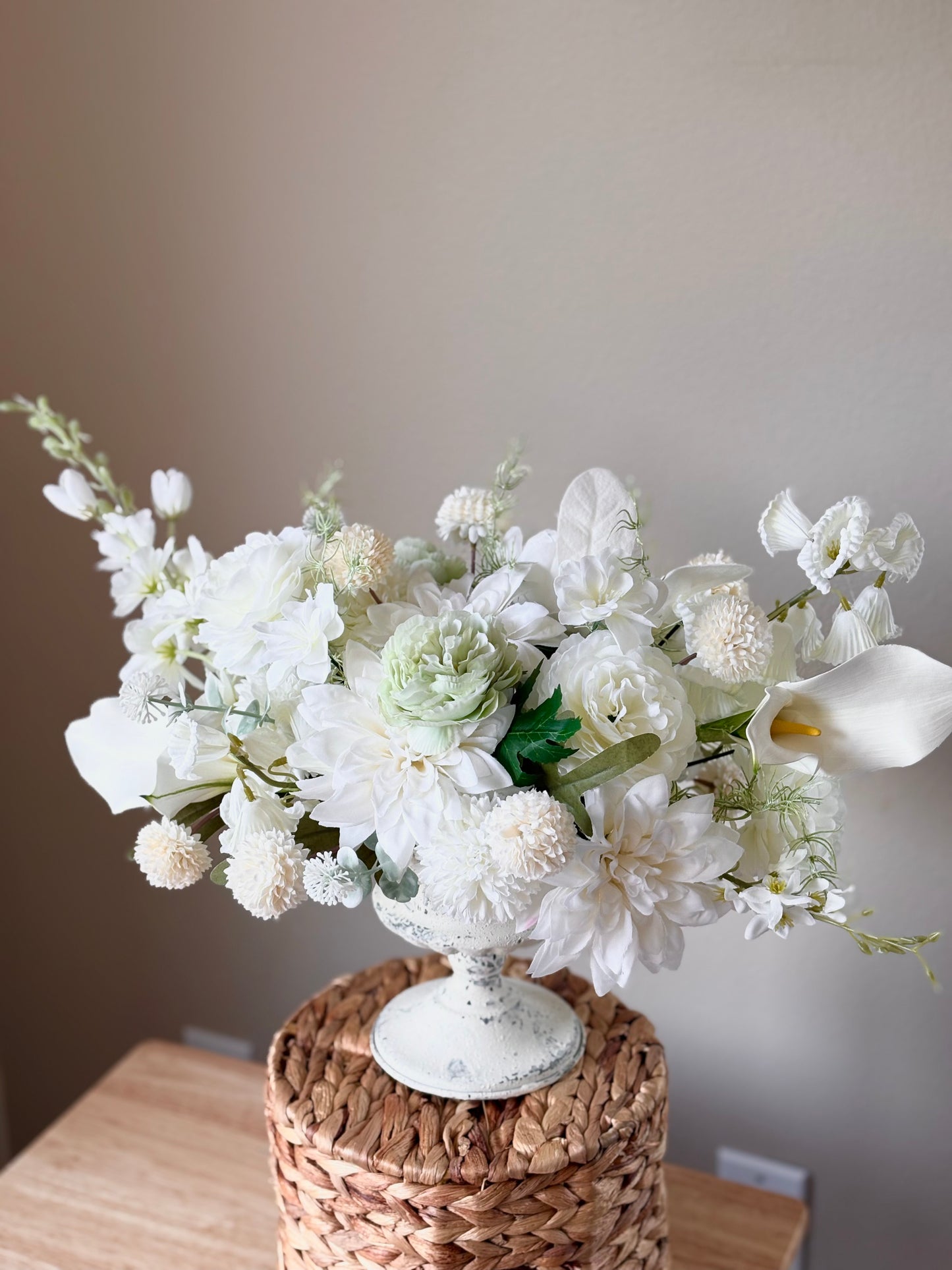 White floral arrangement in a decorative vase on a woven surface with a neutral background
