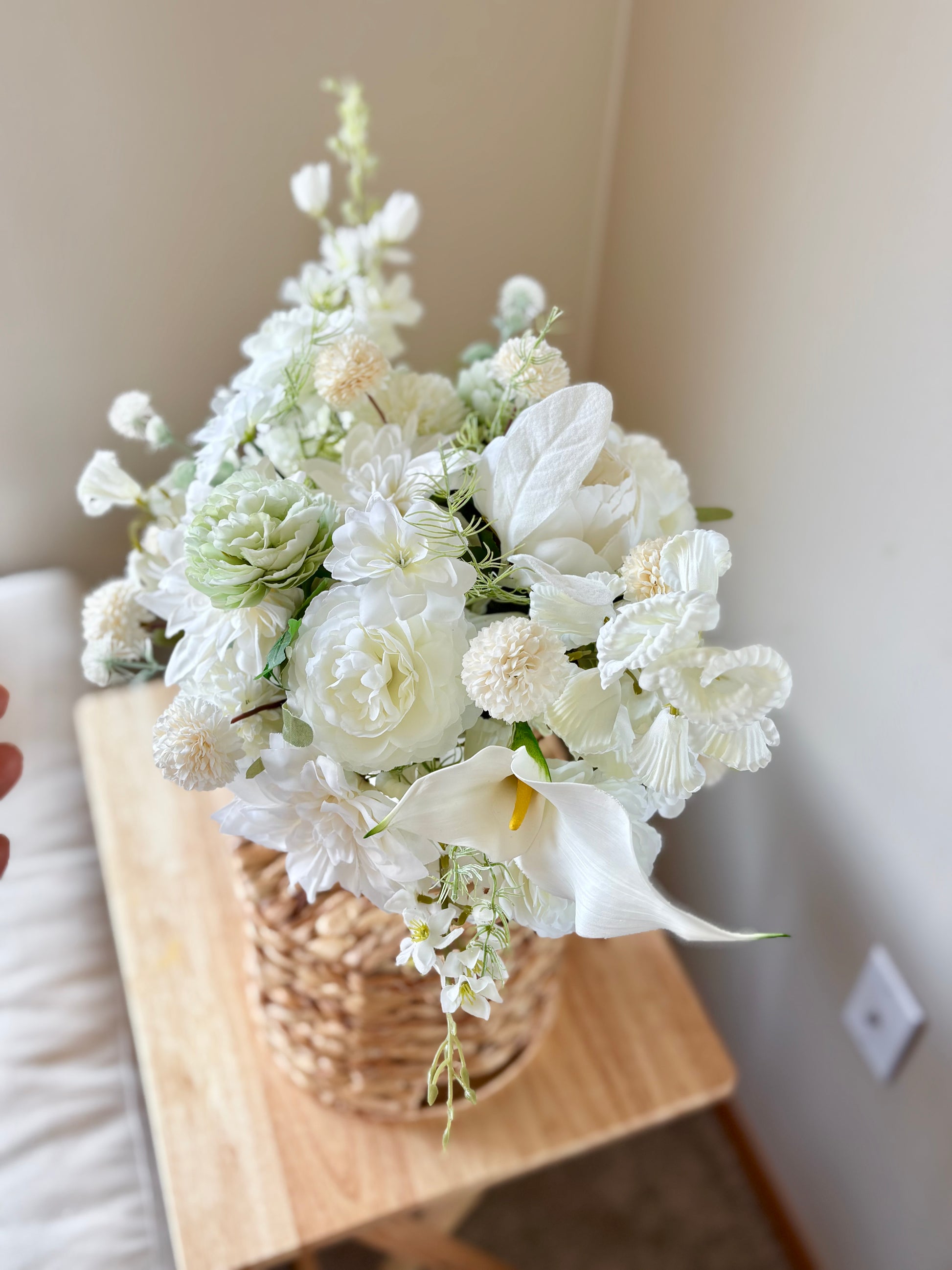 Bouquet of white flowers in a woven basket on a wooden surface.
