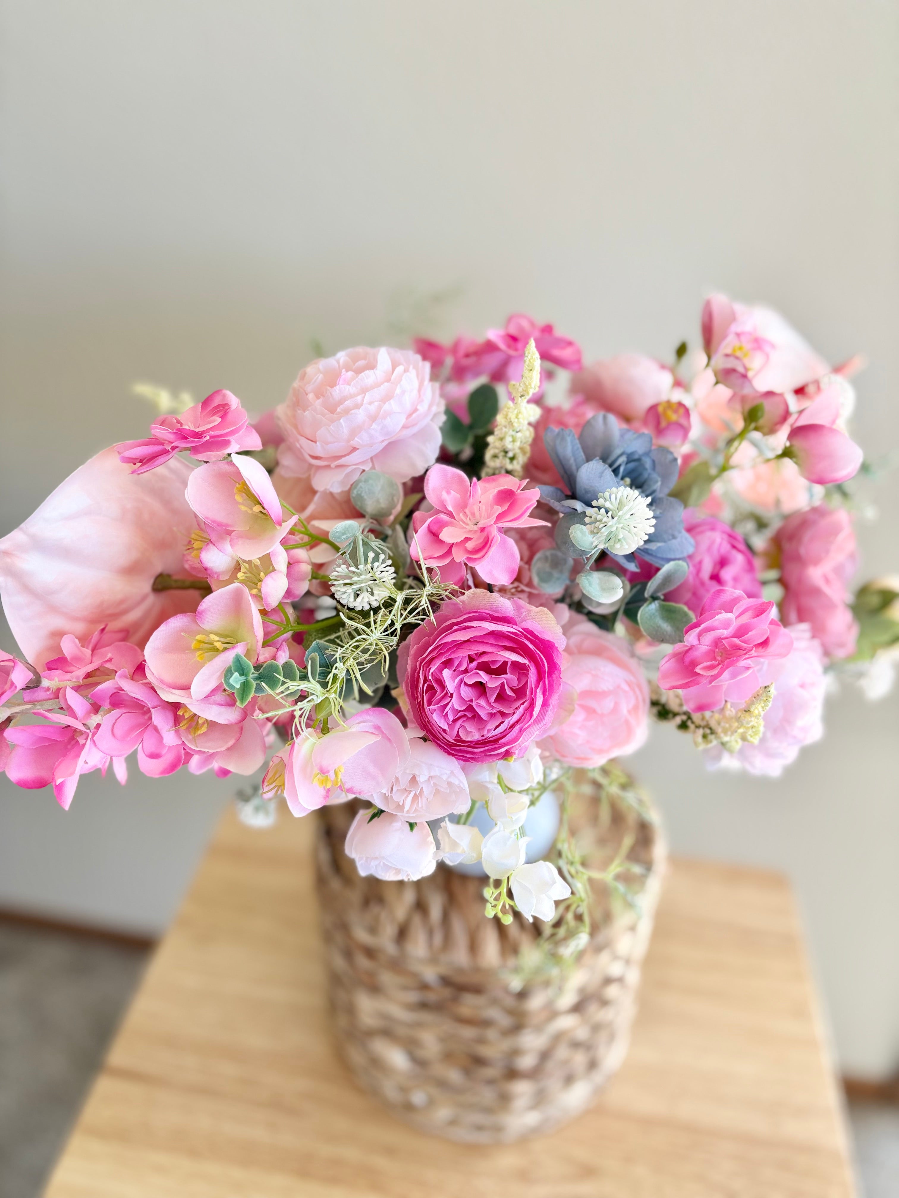 Bouquet of pink flowers in a woven basket on a wooden surface with a neutral background