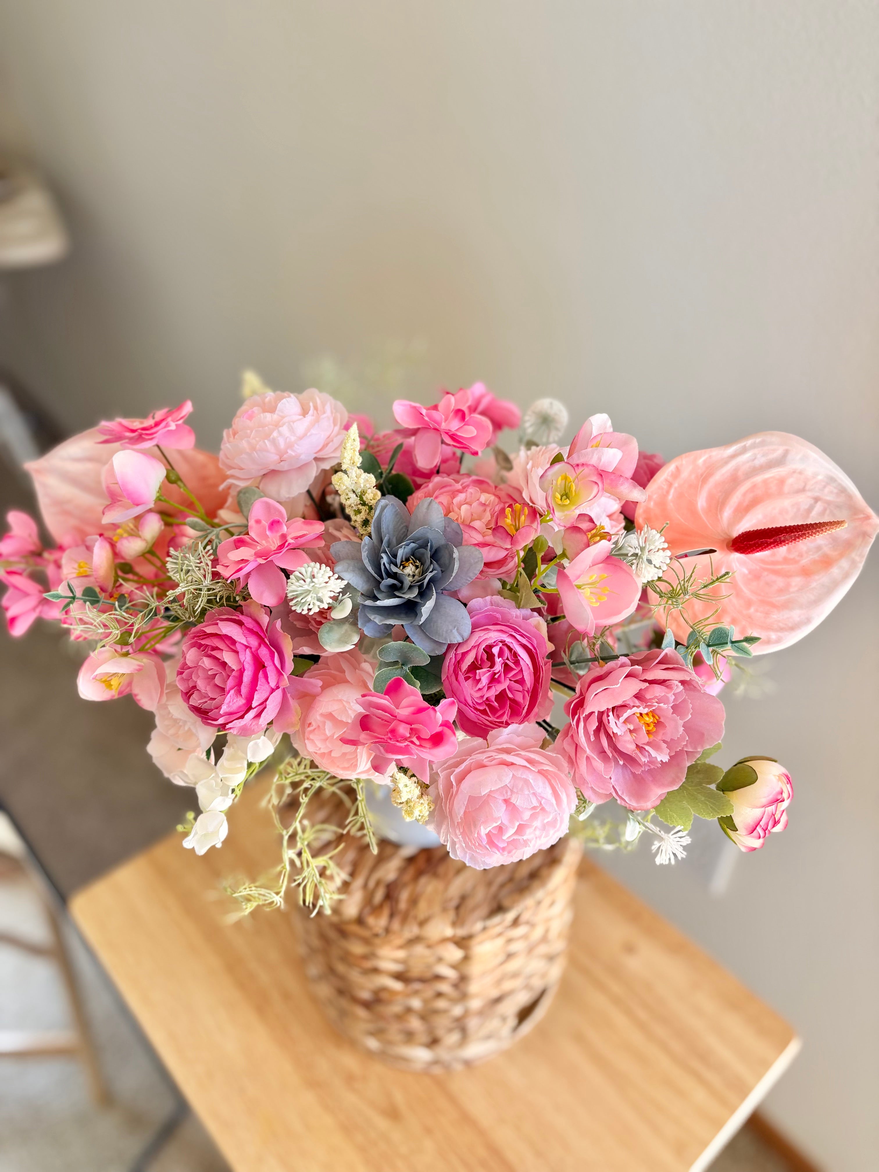 Bouquet of pink flowers in a woven basket on a wooden table.