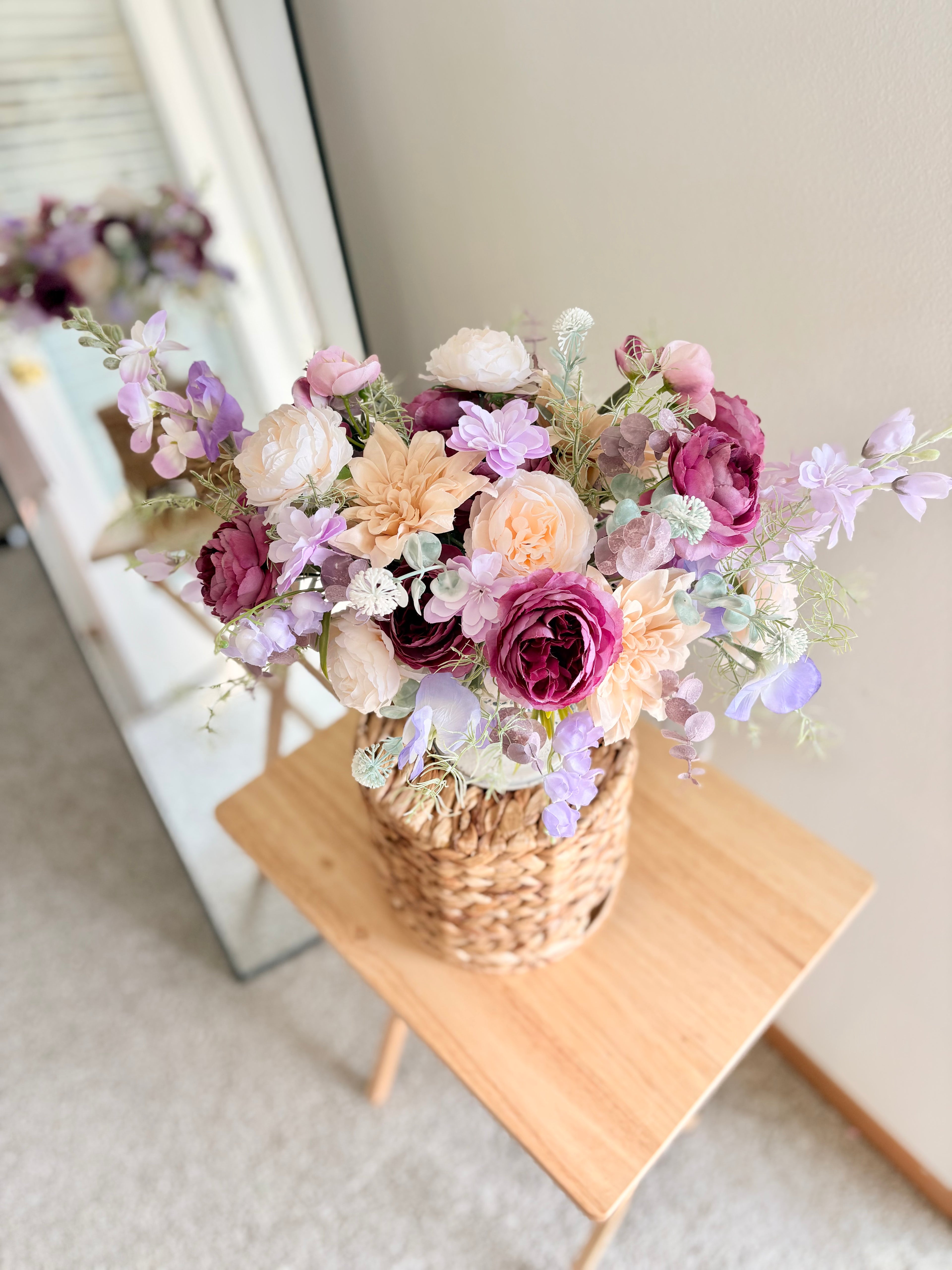 Bouquet of flowers in a woven basket on a wooden stool with a neutral background