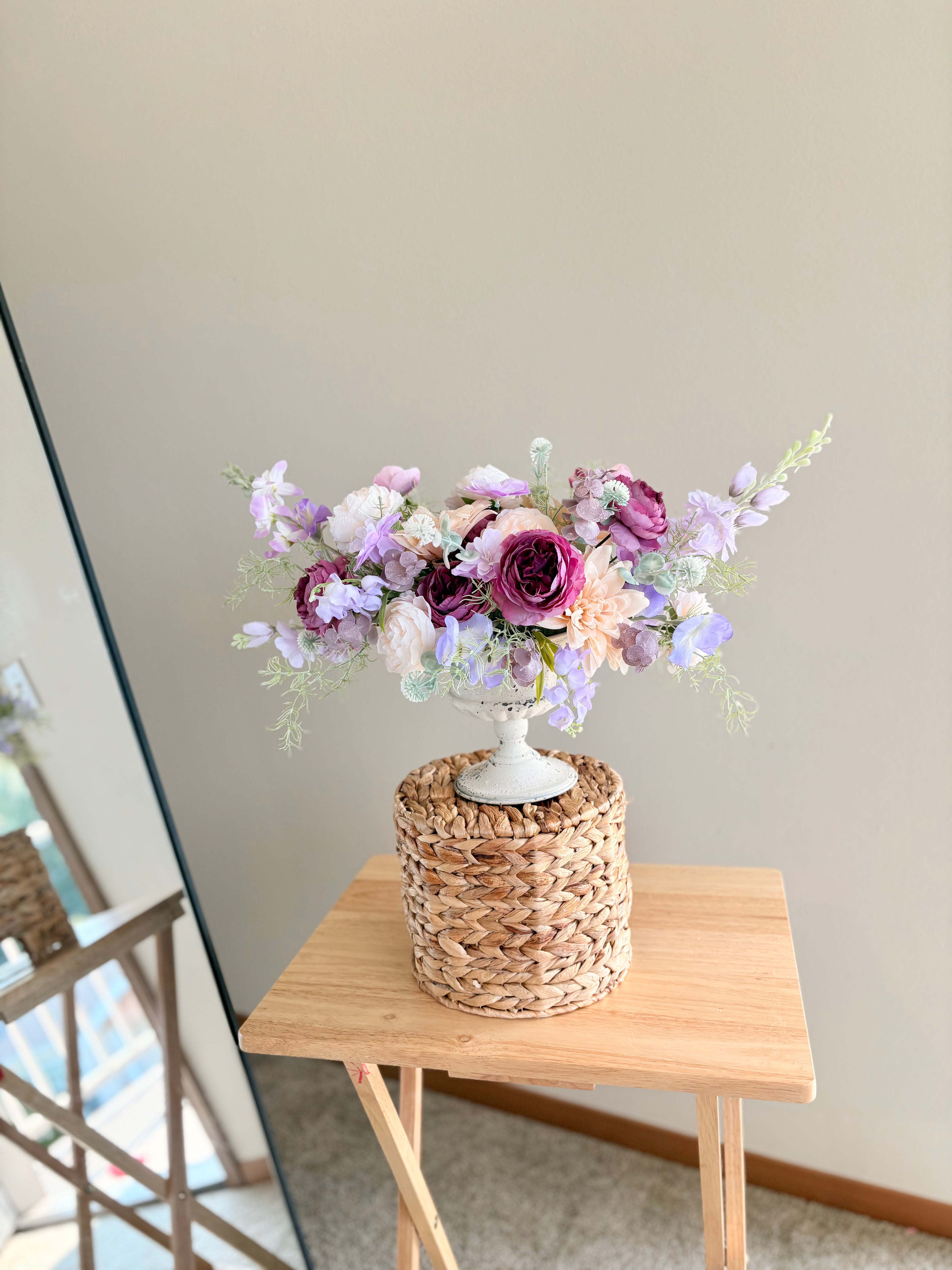 Floral arrangement on a woven basket with a wooden table and light gray wall background