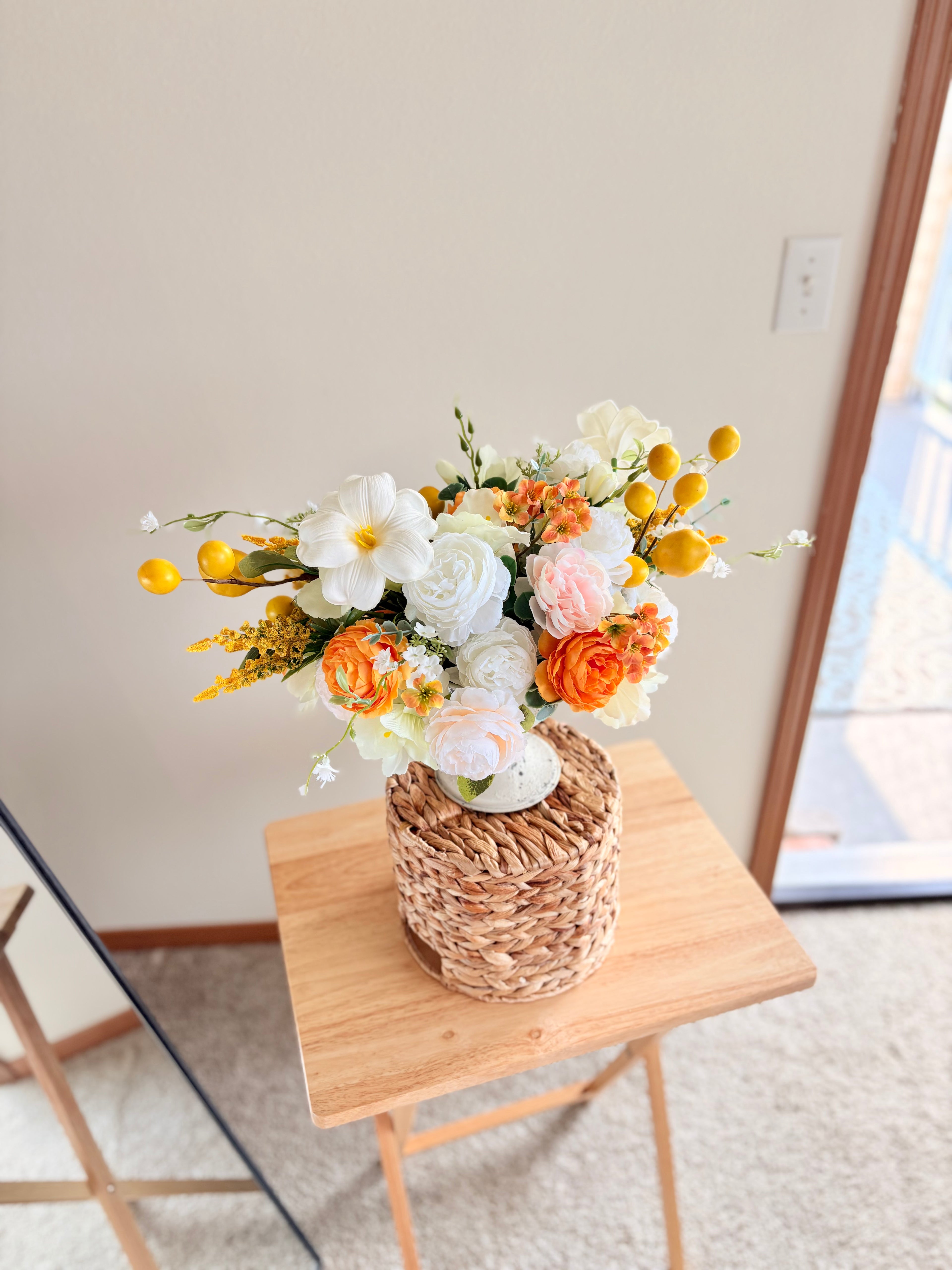 Floral arrangement in a woven basket on a wooden stool with a neutral background