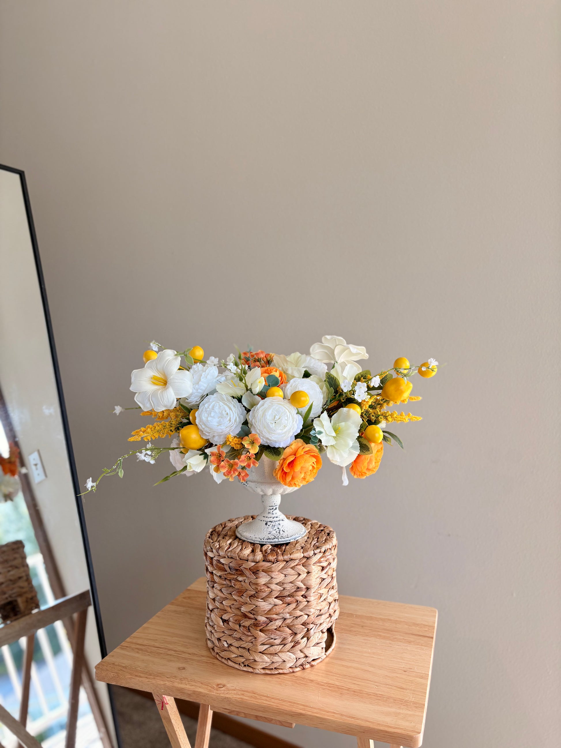 Floral arrangement in a woven basket on a wooden table against a plain wall.