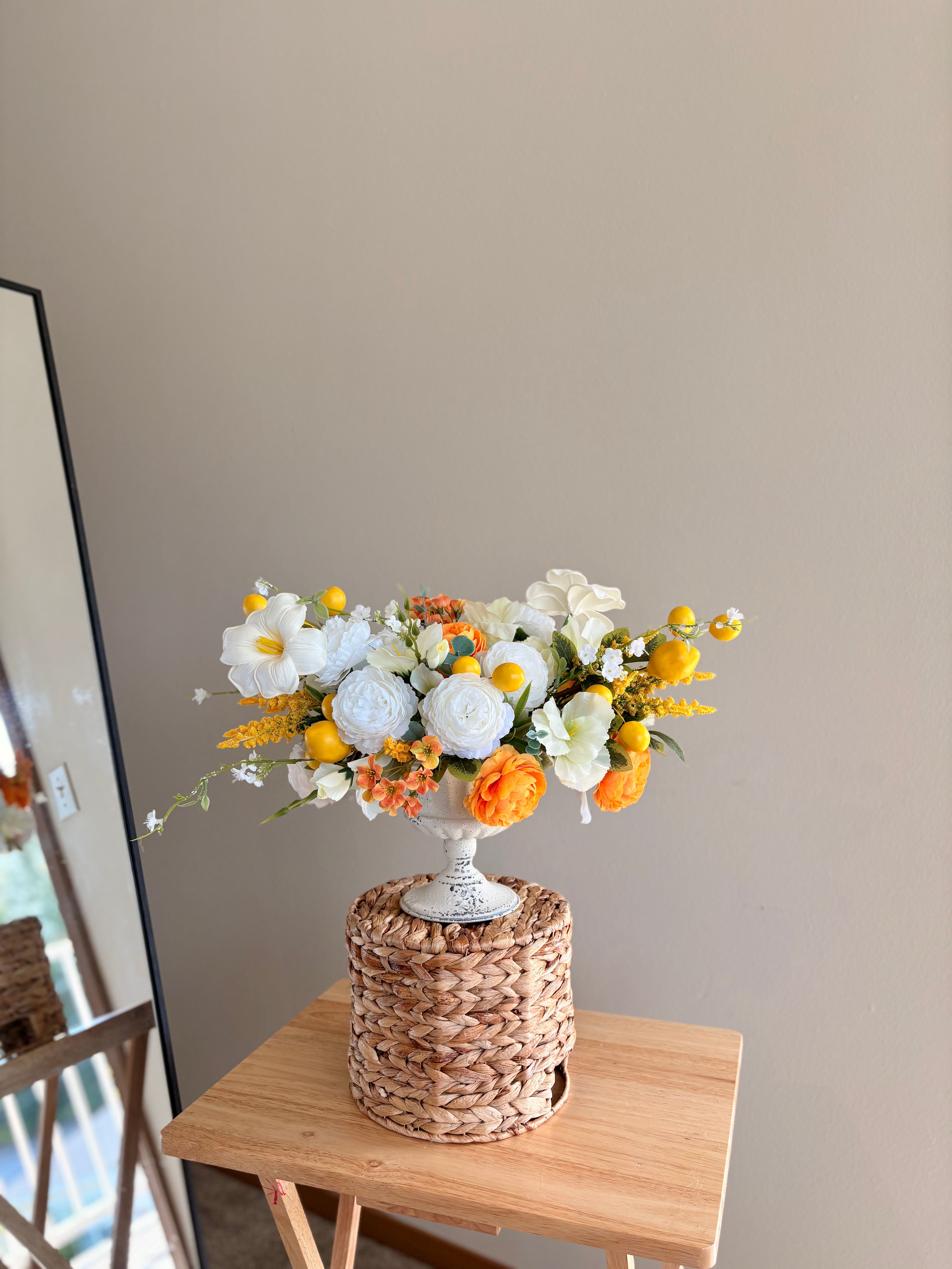 Floral arrangement in a woven basket on a wooden table against a plain wall.